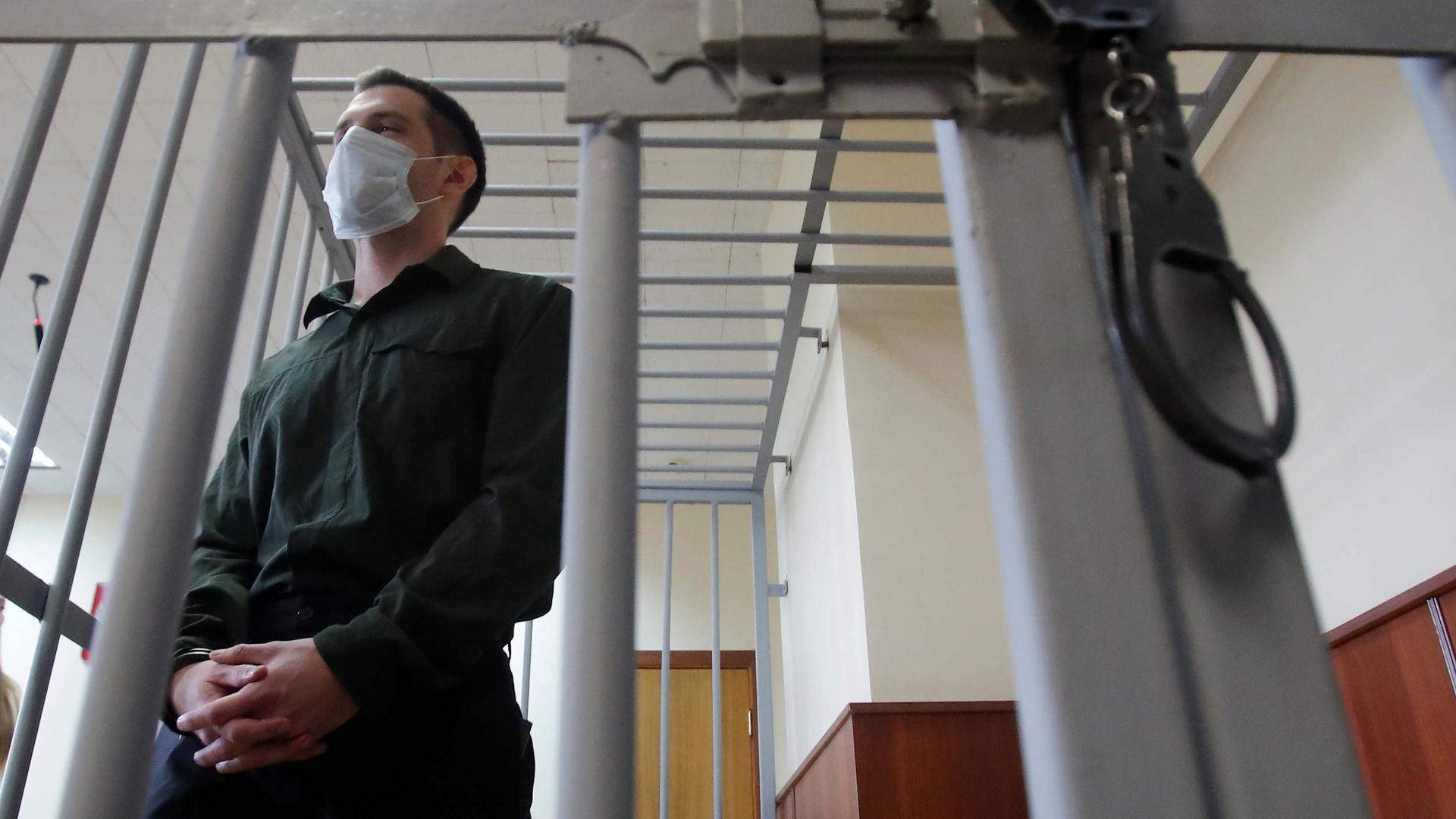 Former US Marine Trevor Reed, who was detained in 2019 and accused of assaulting police officers, stands inside a defendants' cage during a court hearing in Moscow, Russia July 30, 2020.