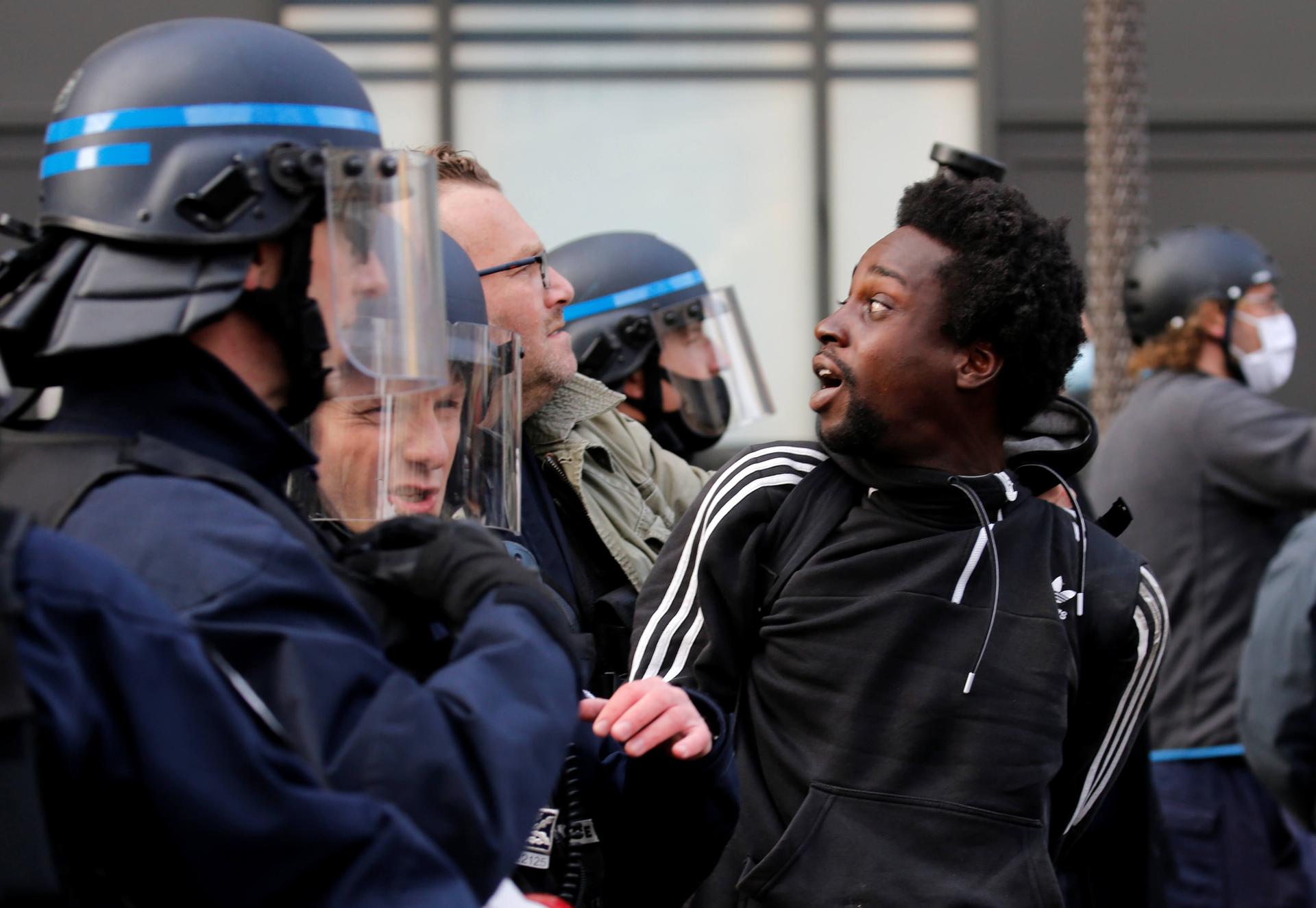 A black Frenchman wearing sweatshirt is detained by a uniformed police offer in France