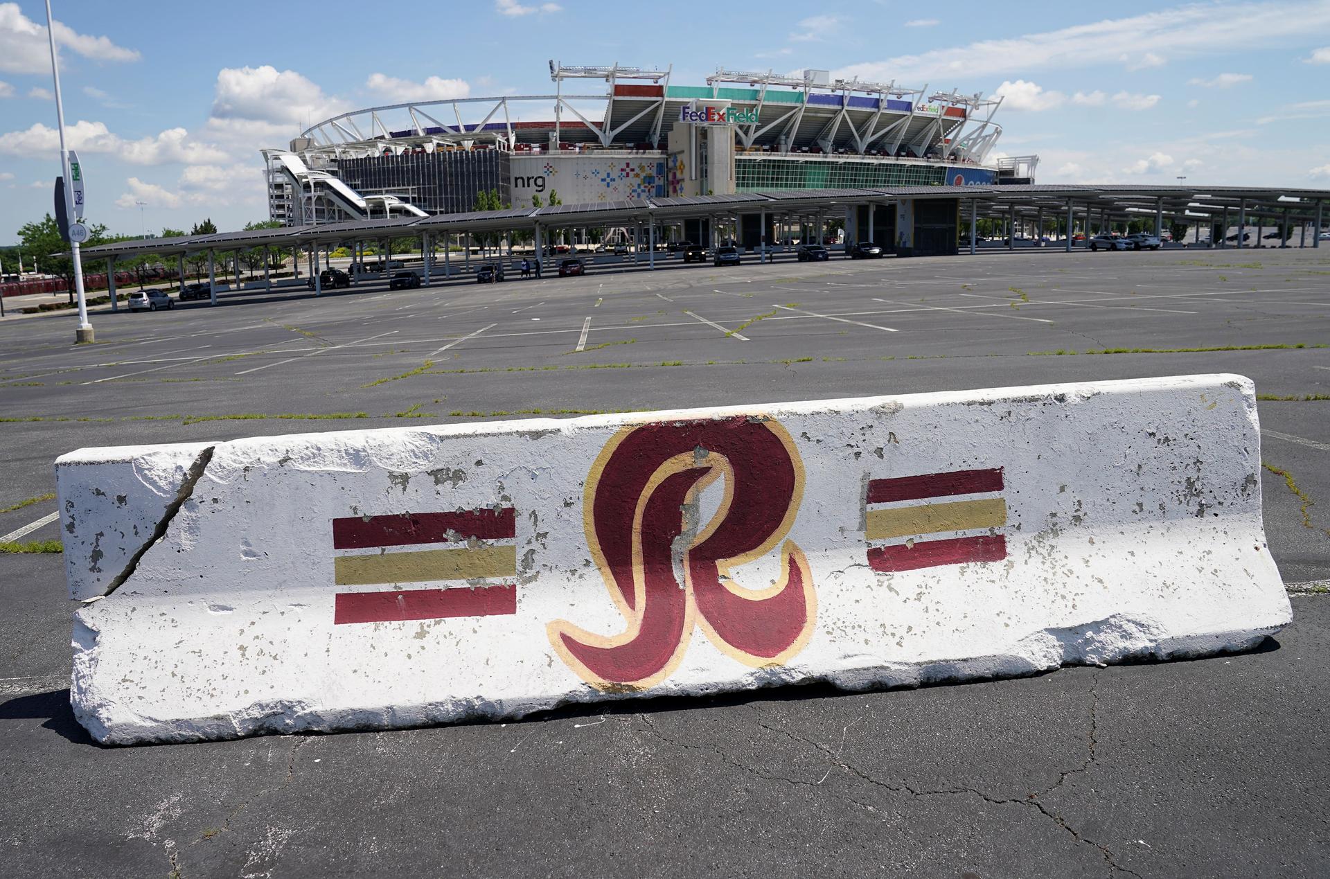 A parking barricade features the red letter R in a parking lot outside of a stadium.