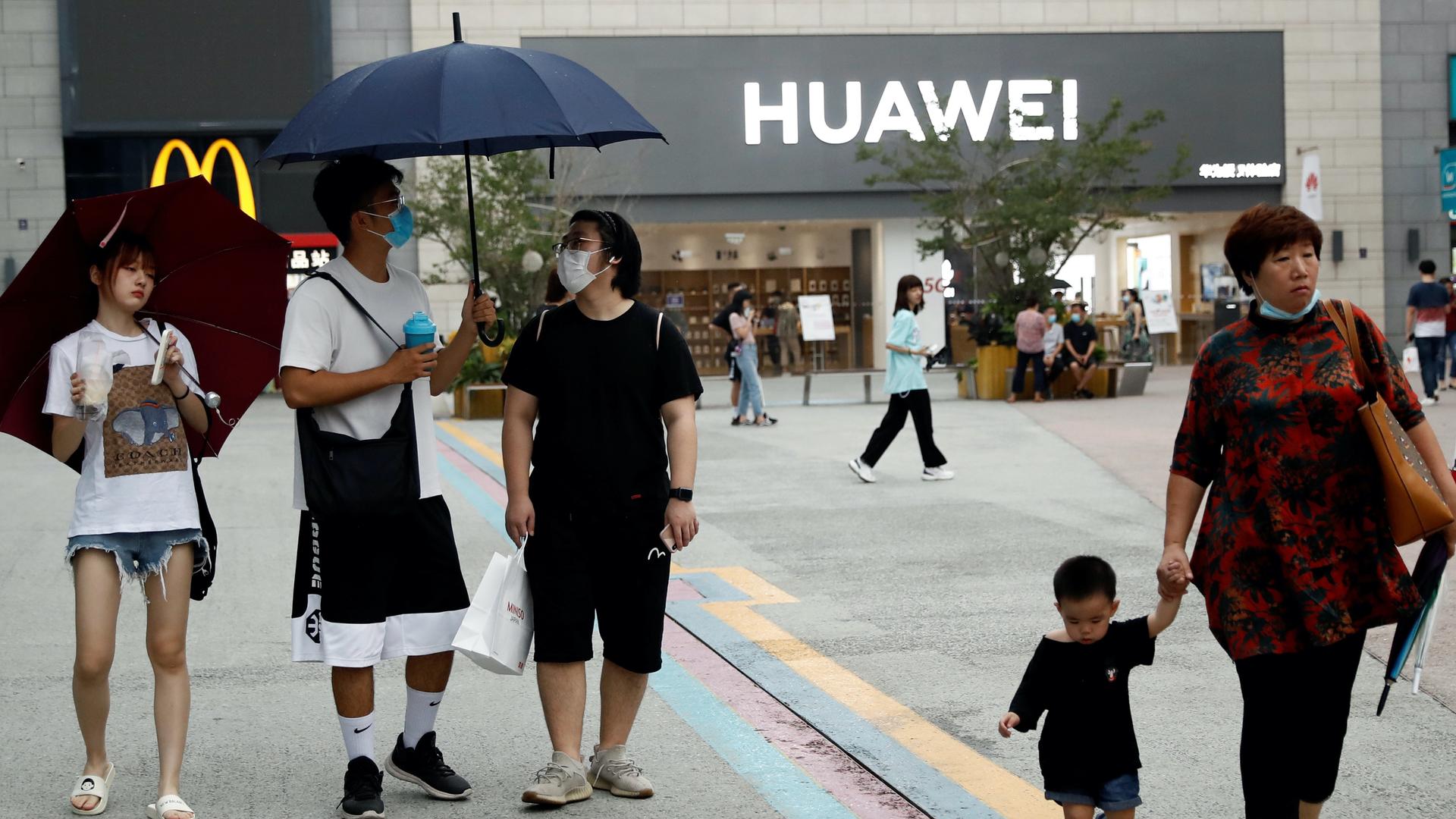 People wear face masks in in Beijing while walking outside near a Huawei store. 