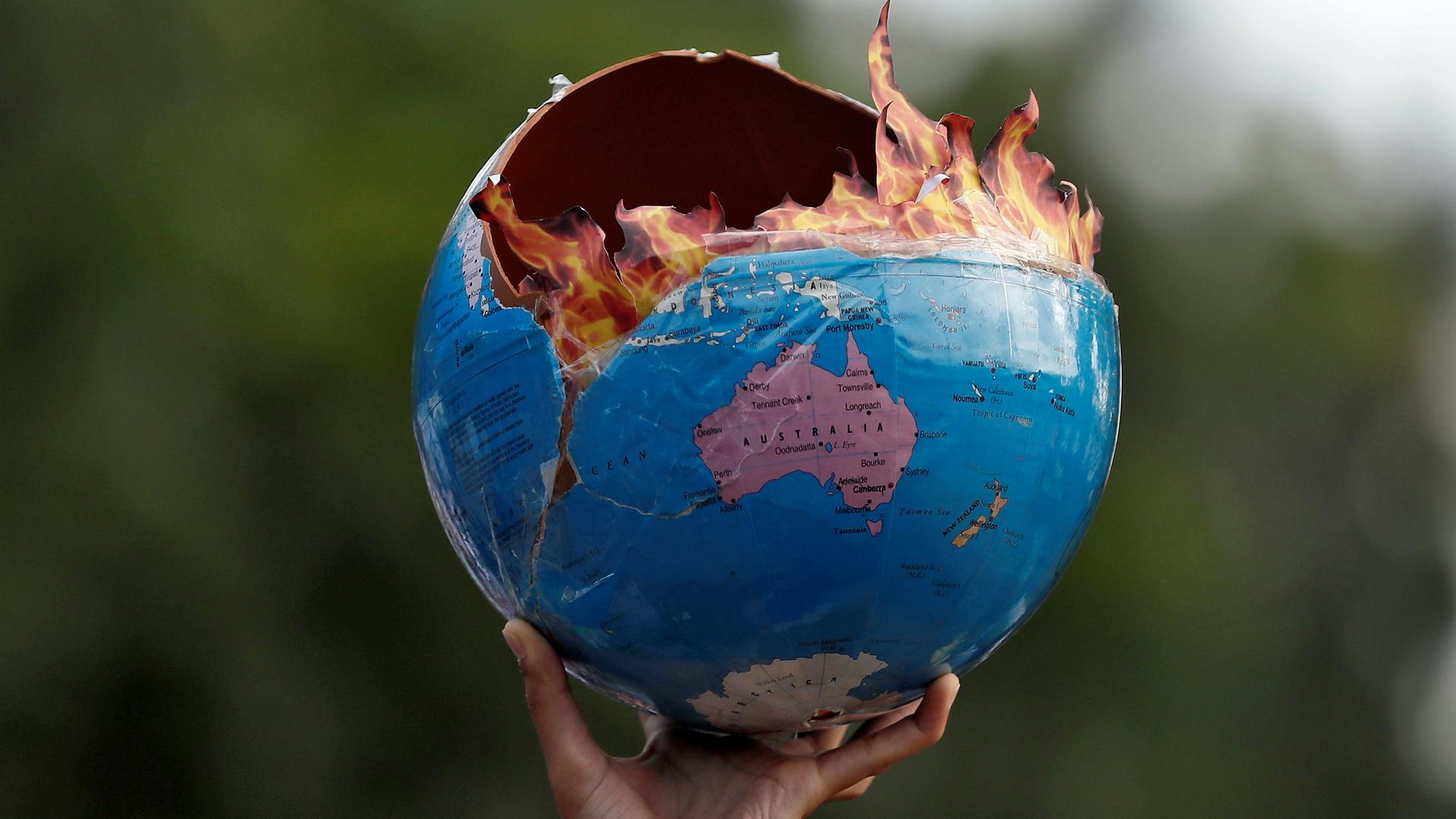 A person holds a replica of a burning globe in the air with fake flames coming out of it. 