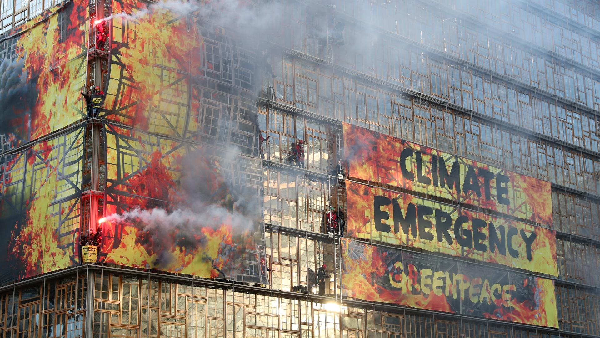 Building reads "climate emergency" with flares of red and orange hues on the front of the building