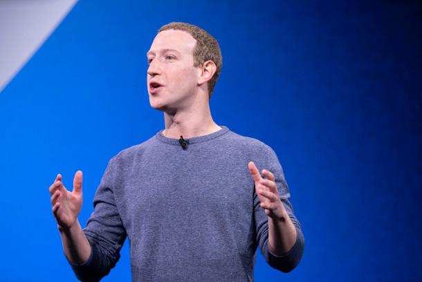 Mark Zuckerberg stands in front of a blue backdrop and speaks on climate misinformation using his hands 