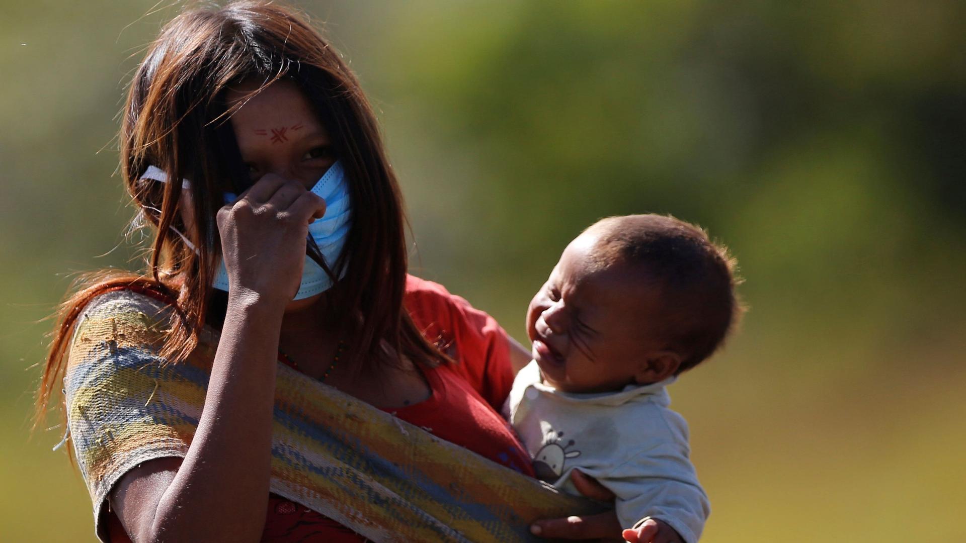 A woman from the Yanomami Indigenous ethnic group wearing protective mask while carrying a child looks on, amid the spread of the coronavirus disease (COVID-19), at the 5th Special Frontier Platoon in the municipality of Auaris, state of Roraima, Brazil, 