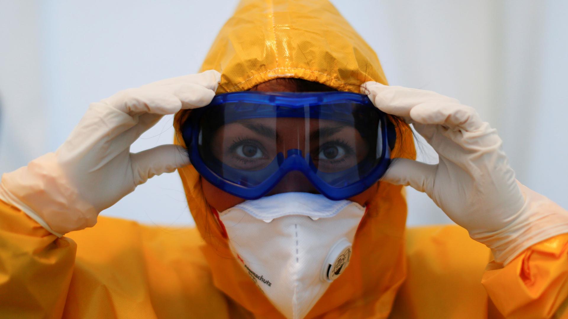 A health care worker is shown in a closeup photographer wearing protective goggles, face mask and a medical gown.