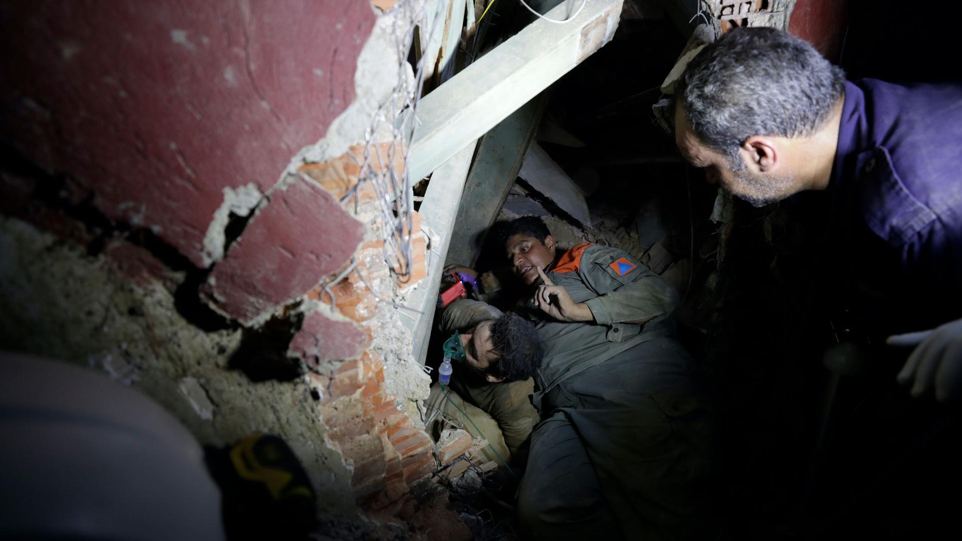 Several people are shown wearing military fatigues and digging through building rubble.