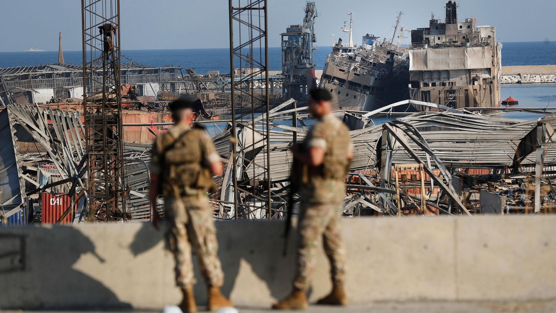 Two soldiers are shown in the near ground in soft focus with widespread rubble from Beirut's destroyed port in the destance.
