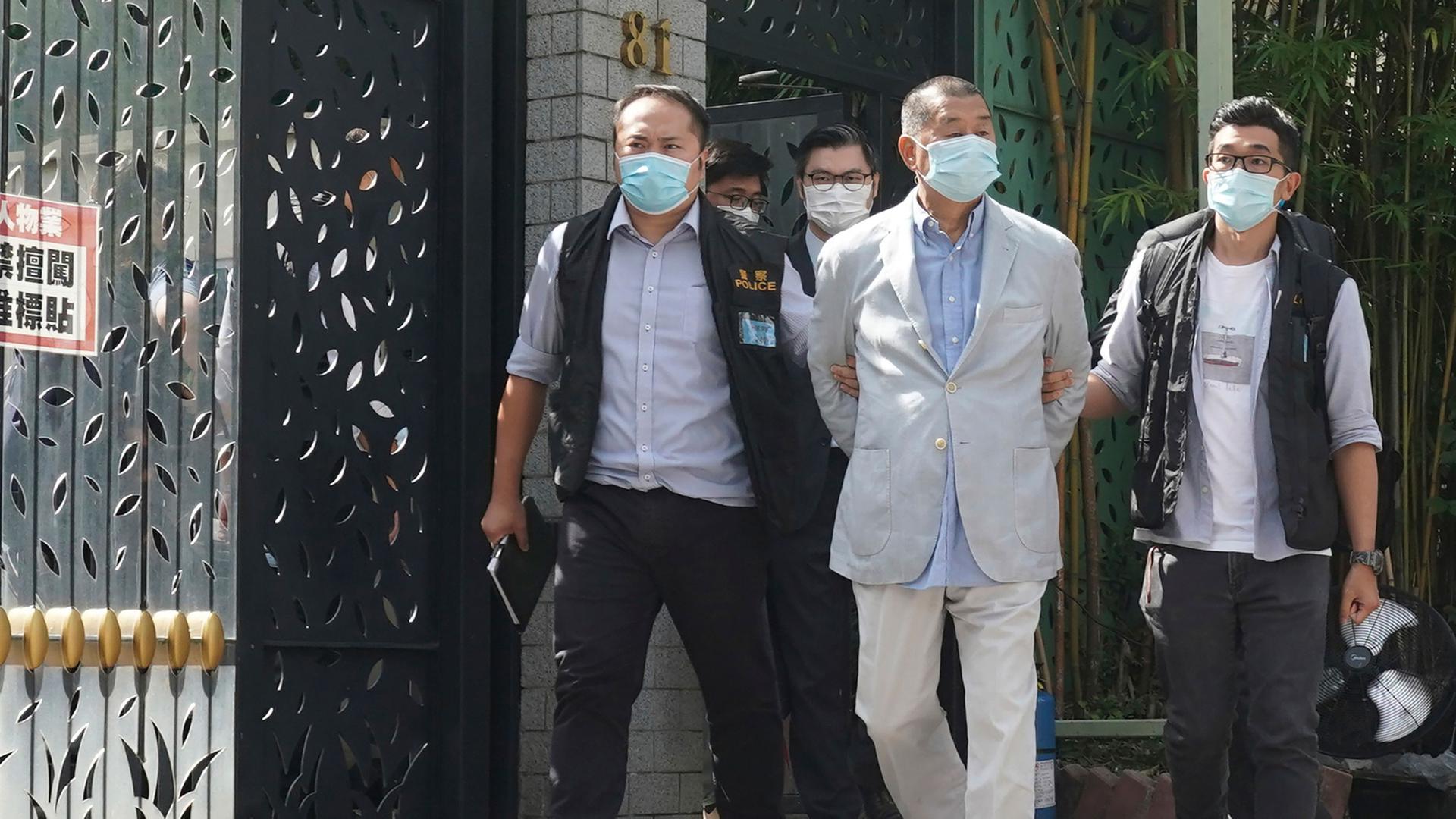 Hong Kong media tycoon Jimmy Lai is shown with his arms tied behind his back and being escorted by four other men all wearing face masks.