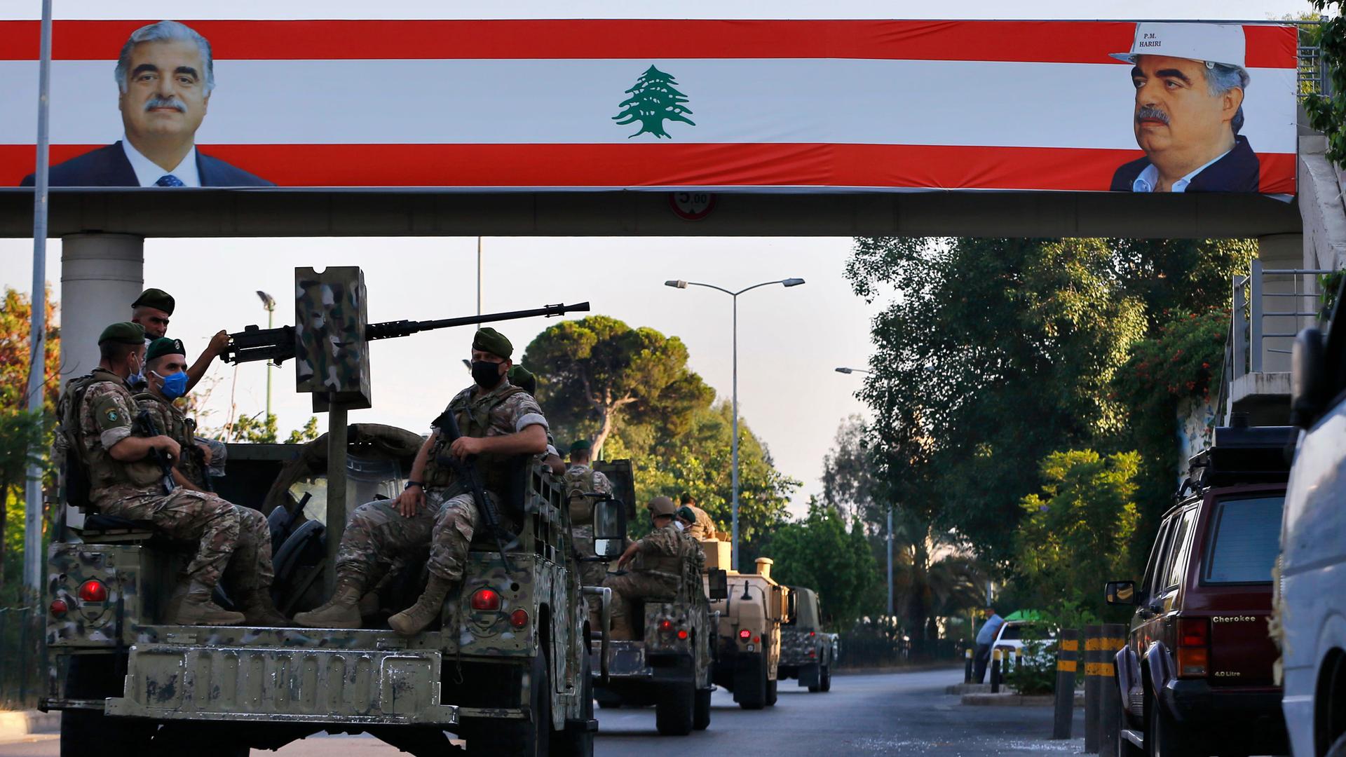 A convoy of military vehicles, some equipped with weapons, pass under a large Lebanese flag with pictures of slain Lebanese Prime Minister Rafik Hariri.