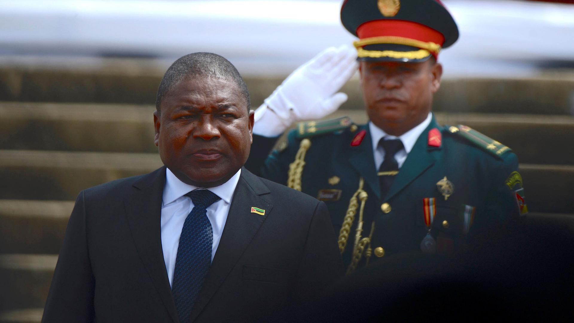 President of Mozambique Filipe Nyusi wears a suit behind a military officer in uniform. 