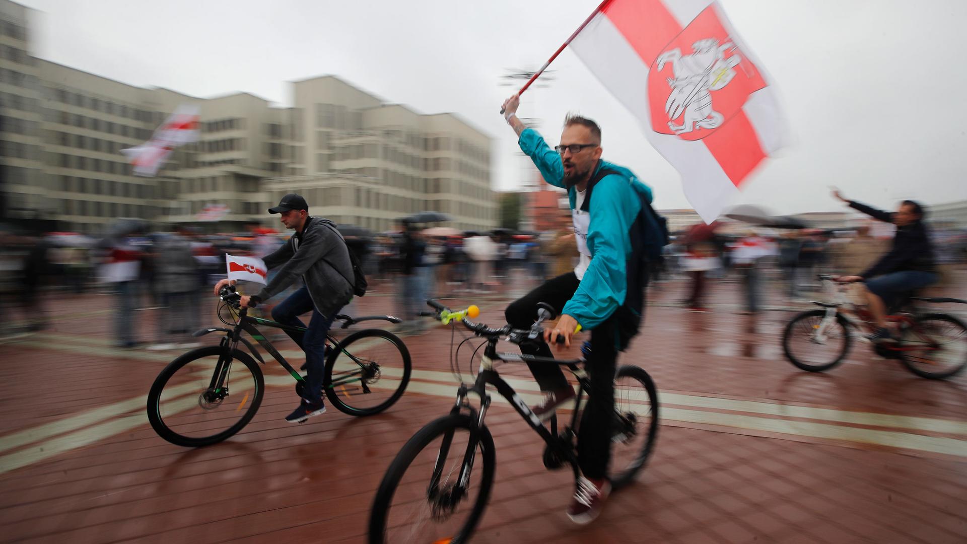 Several people are shown riding bicycles with one carrying an old Belarusian flag in a photograph with blured motion.