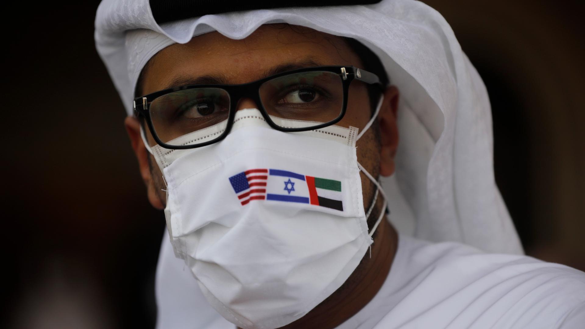 A man wearing a mask bearing the national flags of America, Israel and United Arab Emirates, watches a ceremony after an El Al plane from Israel landed in Abu Dhabi, United Arab Emirates, Aug. 31, 2020. 