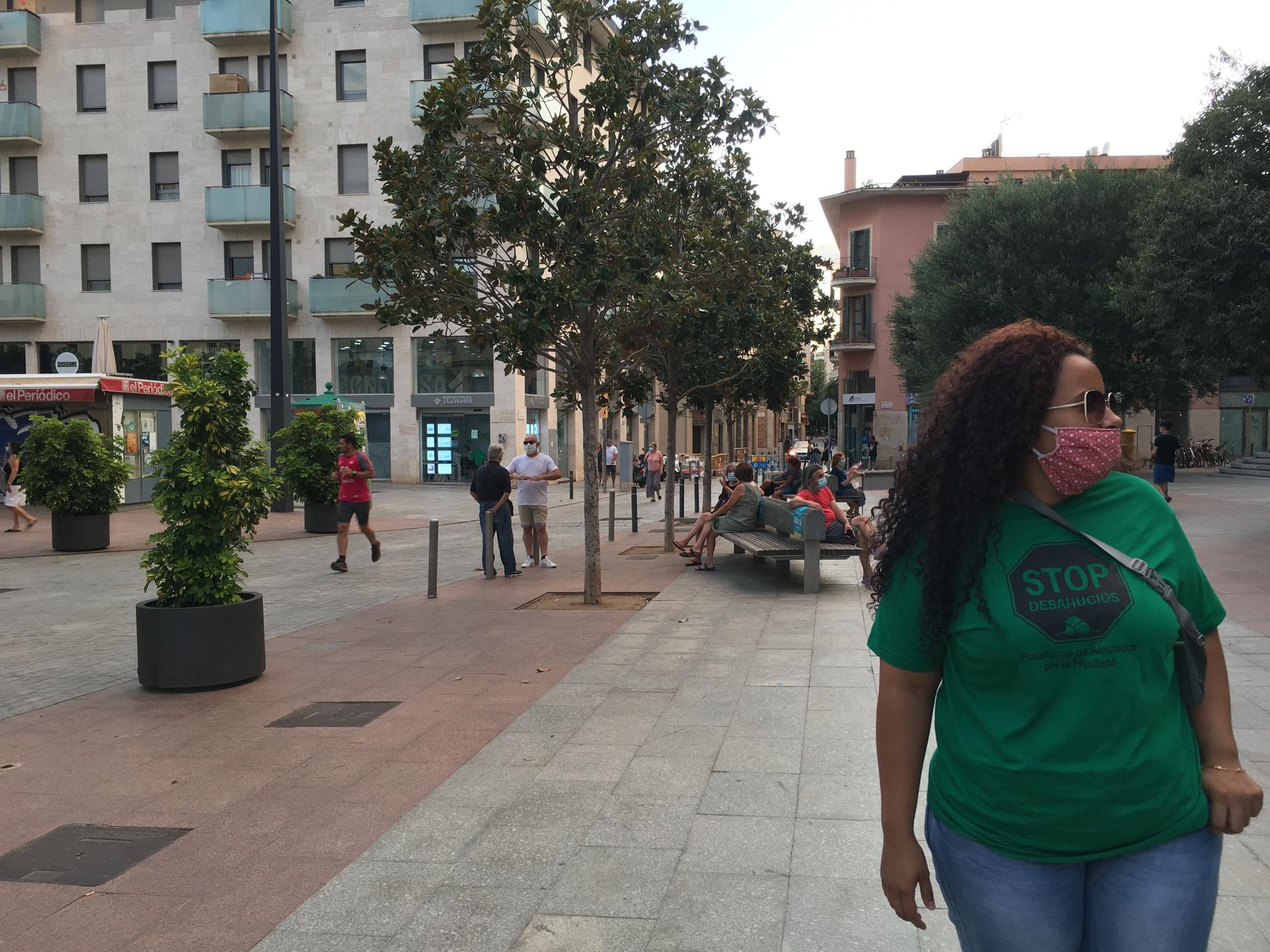 A woman with long brown, curly hair wears a green shirt and jeans as she walks down an urban street.
