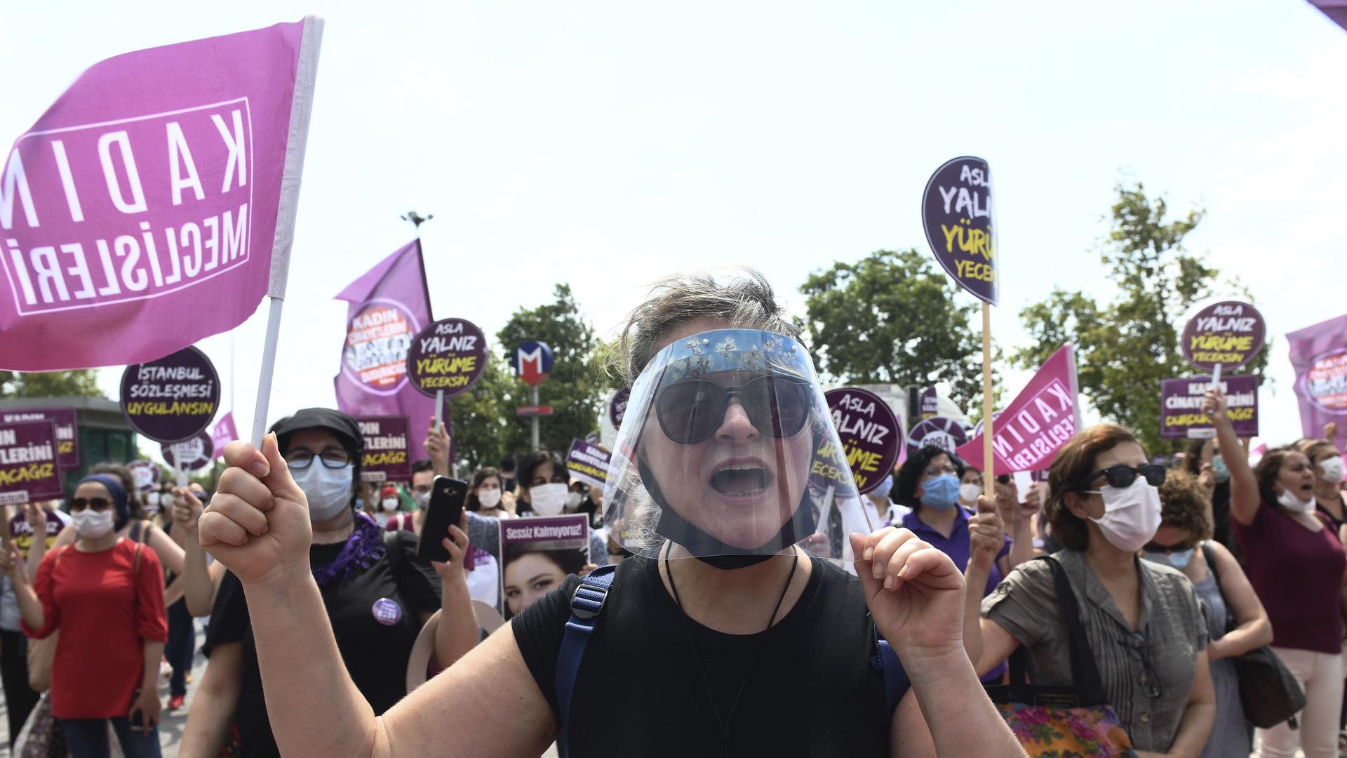 Women hold protest signs and also wear face masks and plastic shields as they protest. 