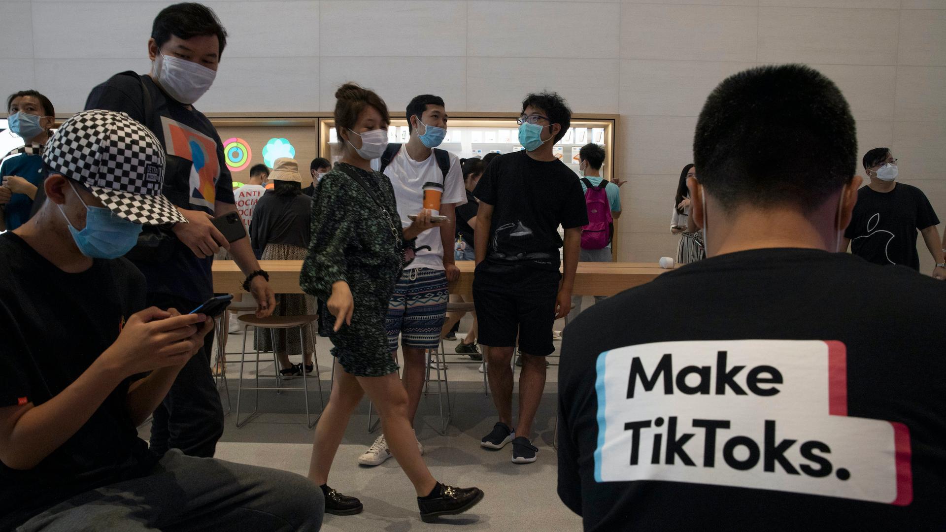 Several people are shown in an Apple store in Beijing with one person in the near ground wearing a t-shirt with "Make TikToks" printed on it.