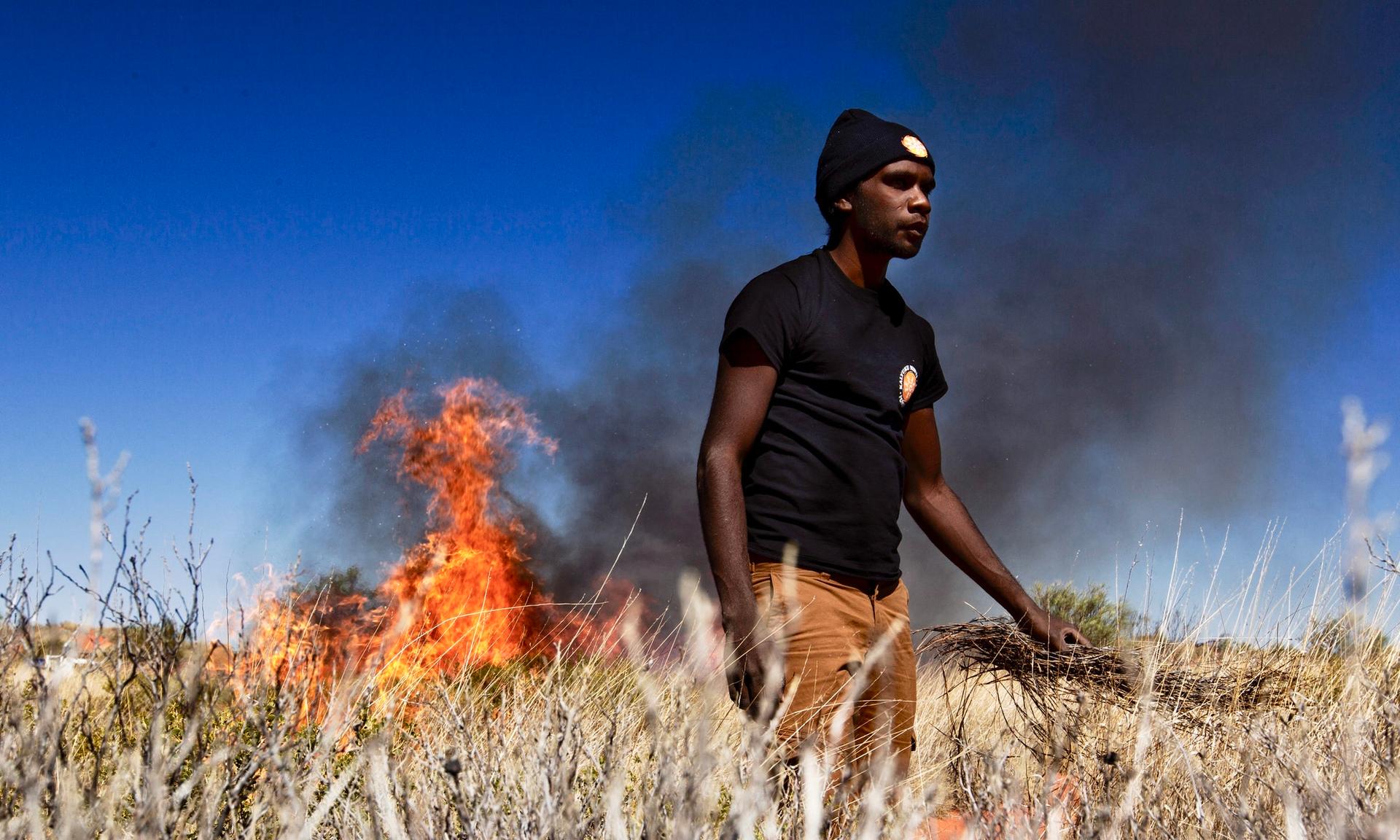 An Aboriginal fire ranger standing in front of a burning bushfire