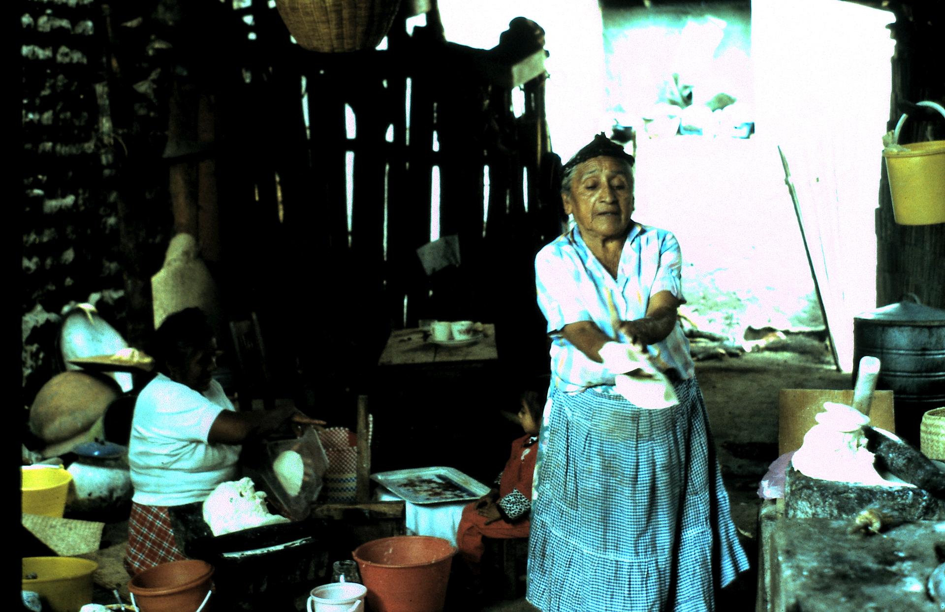 A woman stands up while molding tamales with her hands.
