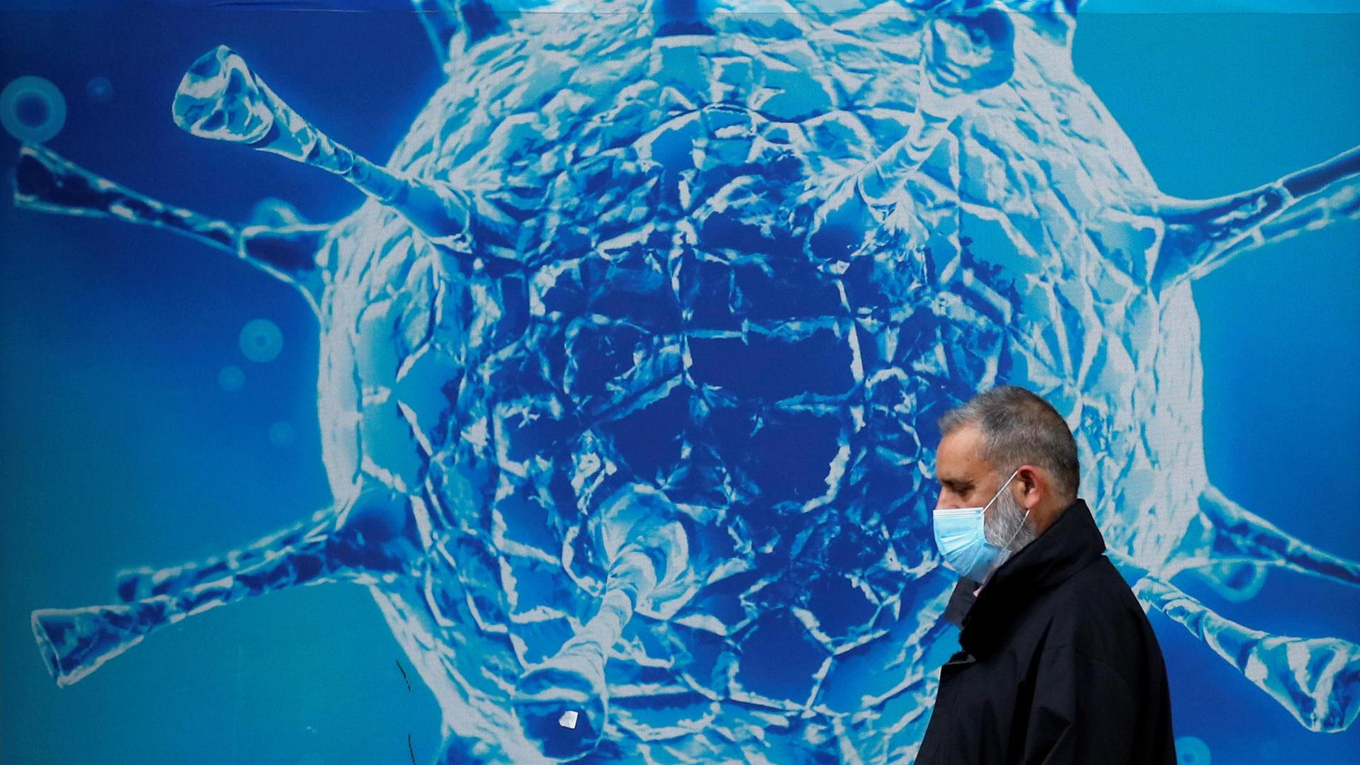 A man wearing a protective face mask walks past an illustration of a virus outside a regional science centre amid the coronavirus disease (COVID-19) outbreak, in Oldham, Britain, August 3, 2020.