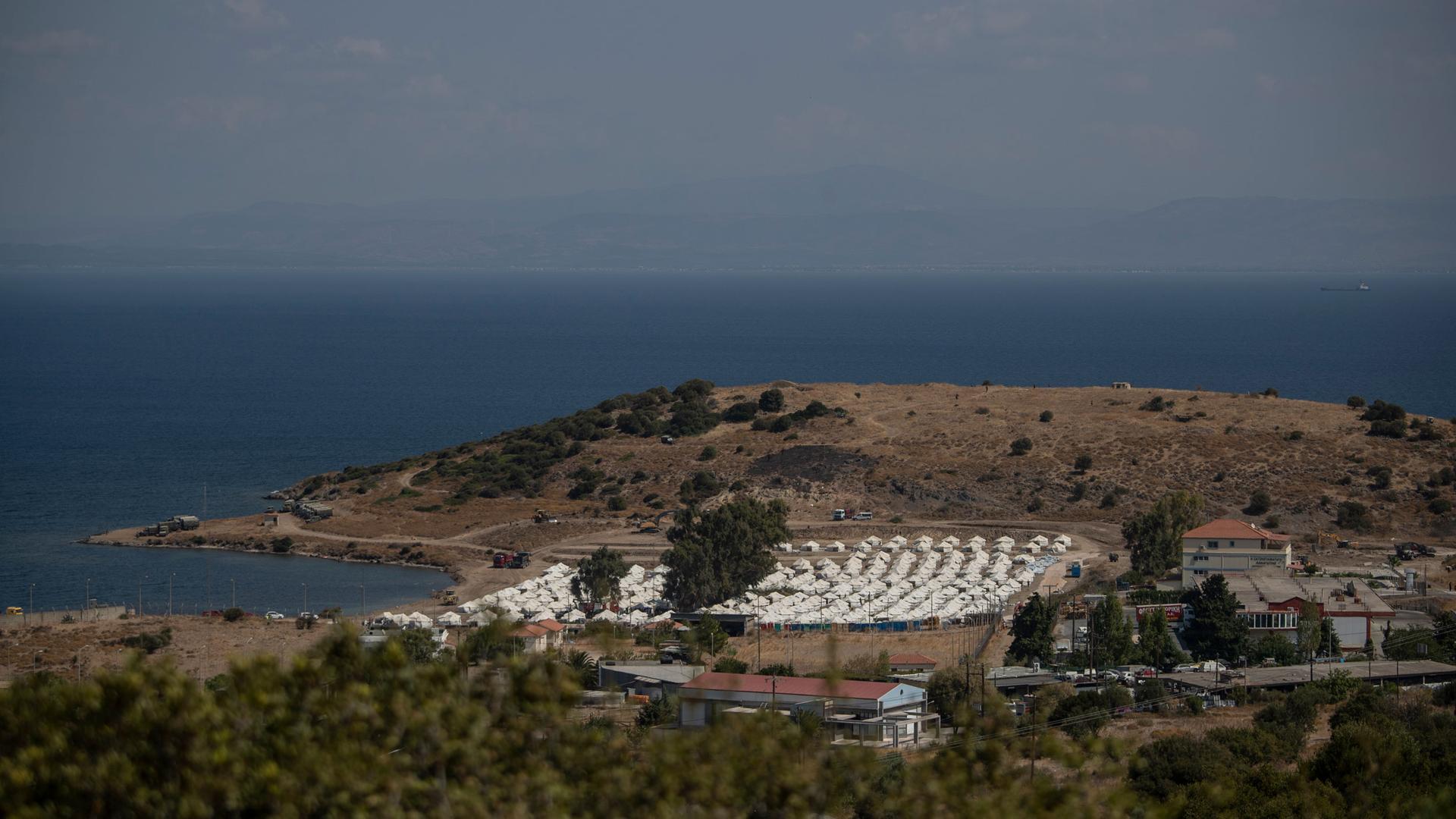A view of a newly constructed camp for asylum-seekers with dozens of rows of white tents and the Aegan Sea in the distance.