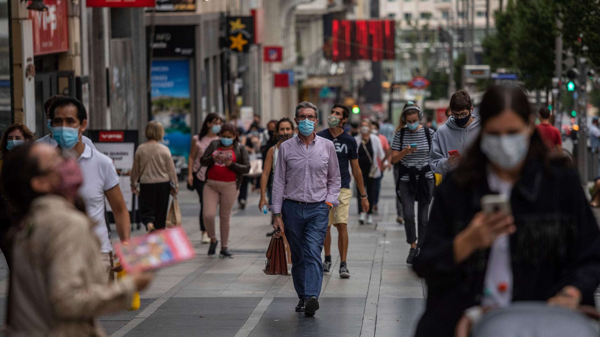 Dozens of people are show walking around a shopping district and wearing face masks in Madrid, Spain.
