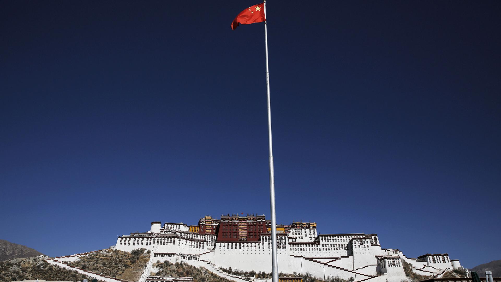 China's red flag is show flying on a pole with the large white facade of the Potala Palace in the distance.