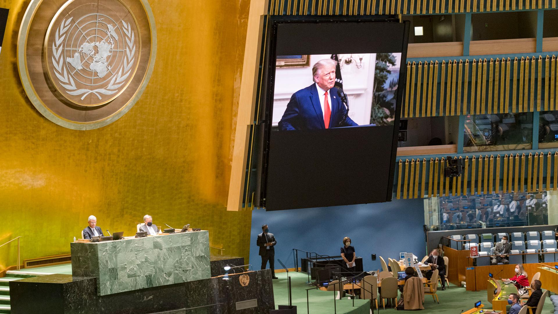 US President Donald Trump, shown on a large video screen against a gold leaf wall and the United Nations symbol.