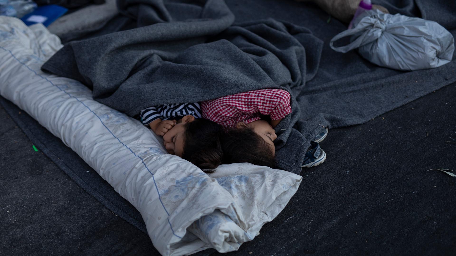 Two children sleep beneath gray blankets on the road near the Moria refugee camp on the northeastern island of Lesbos, Greece, Sept. 10, 2020. 