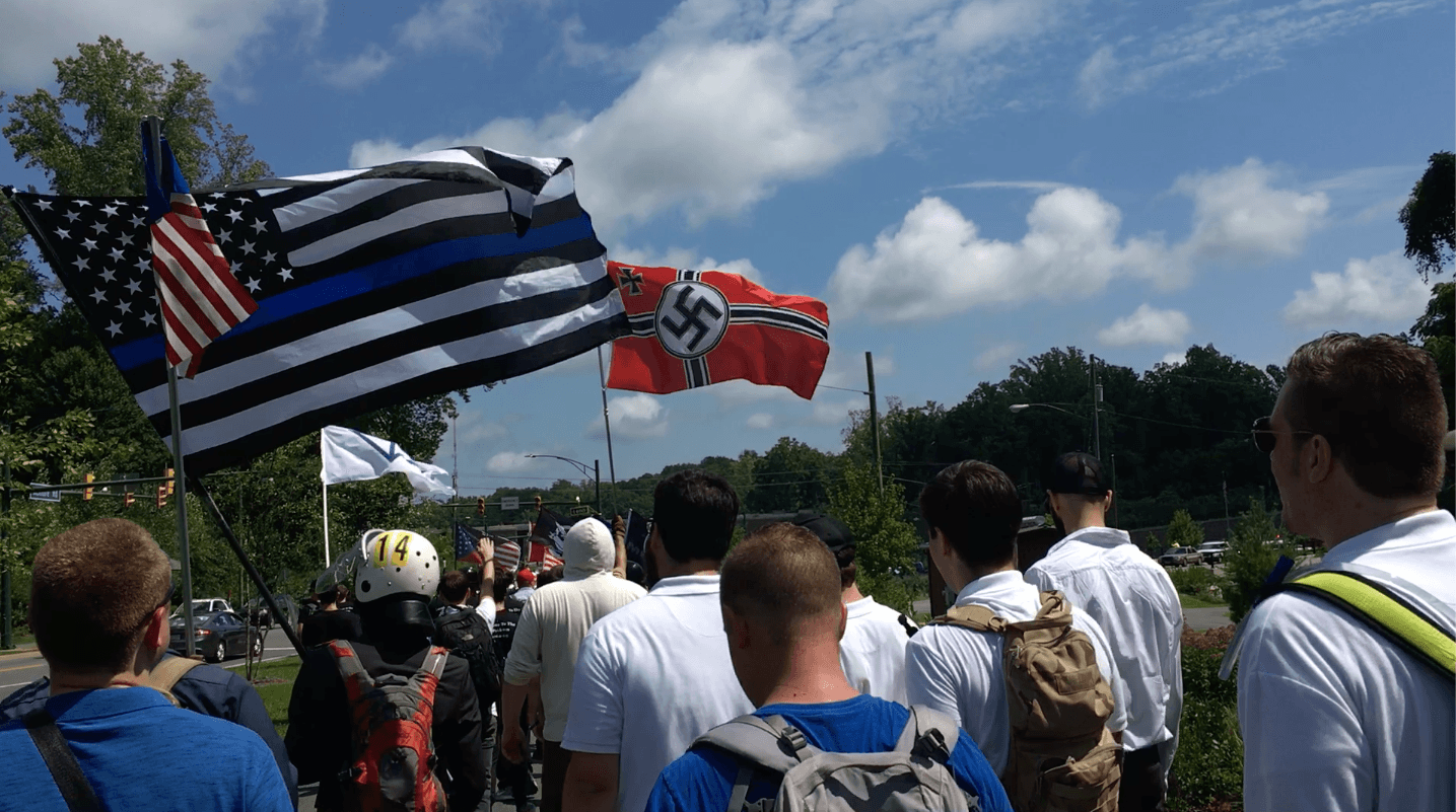 White men walk down a street with white power flags showing Nazi symbols