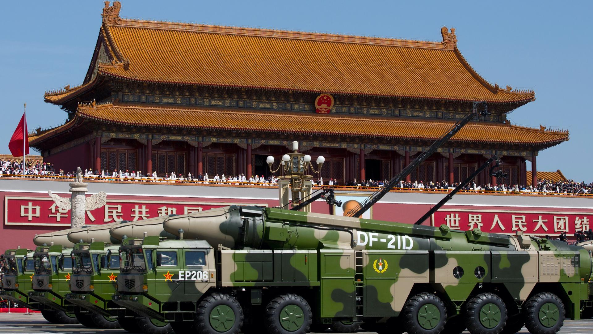 Military tanks pass by a building featuring traditional Chinese architecture. 