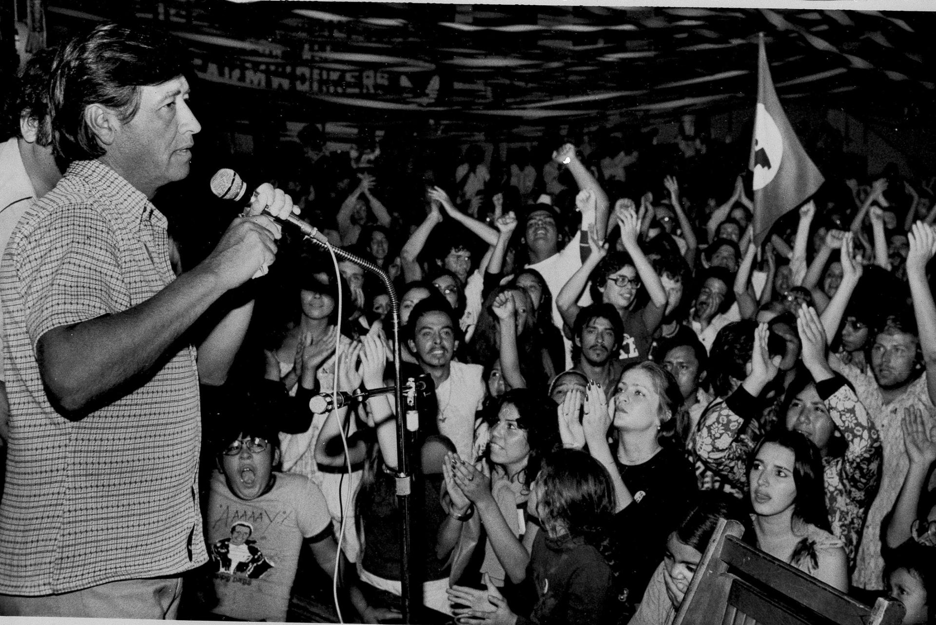 Una fotografia de Cesar Chavez hablando en frente a un grupo de personas.