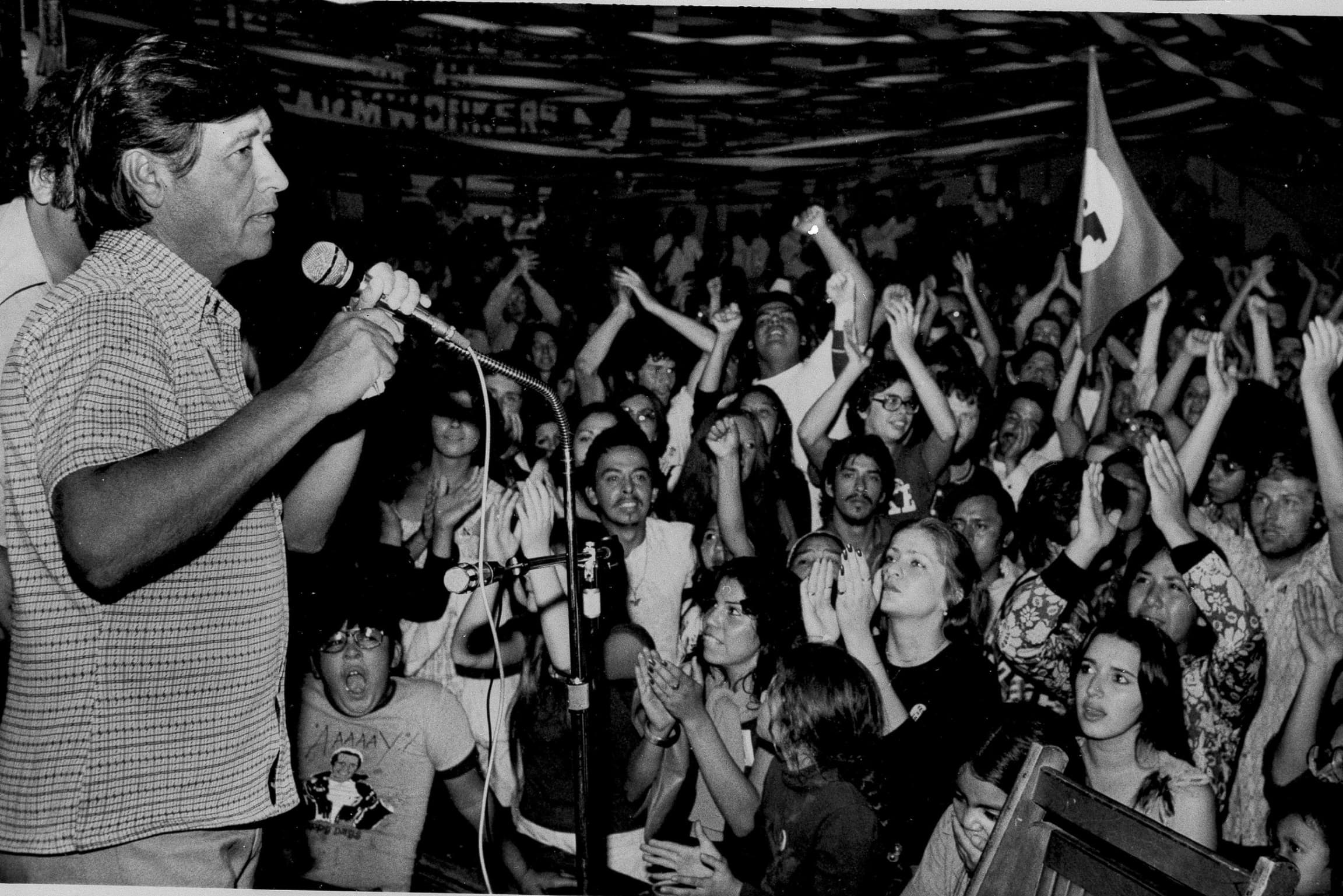 Una fotografia de Cesar Chavez hablando en frente a un grupo de personas.