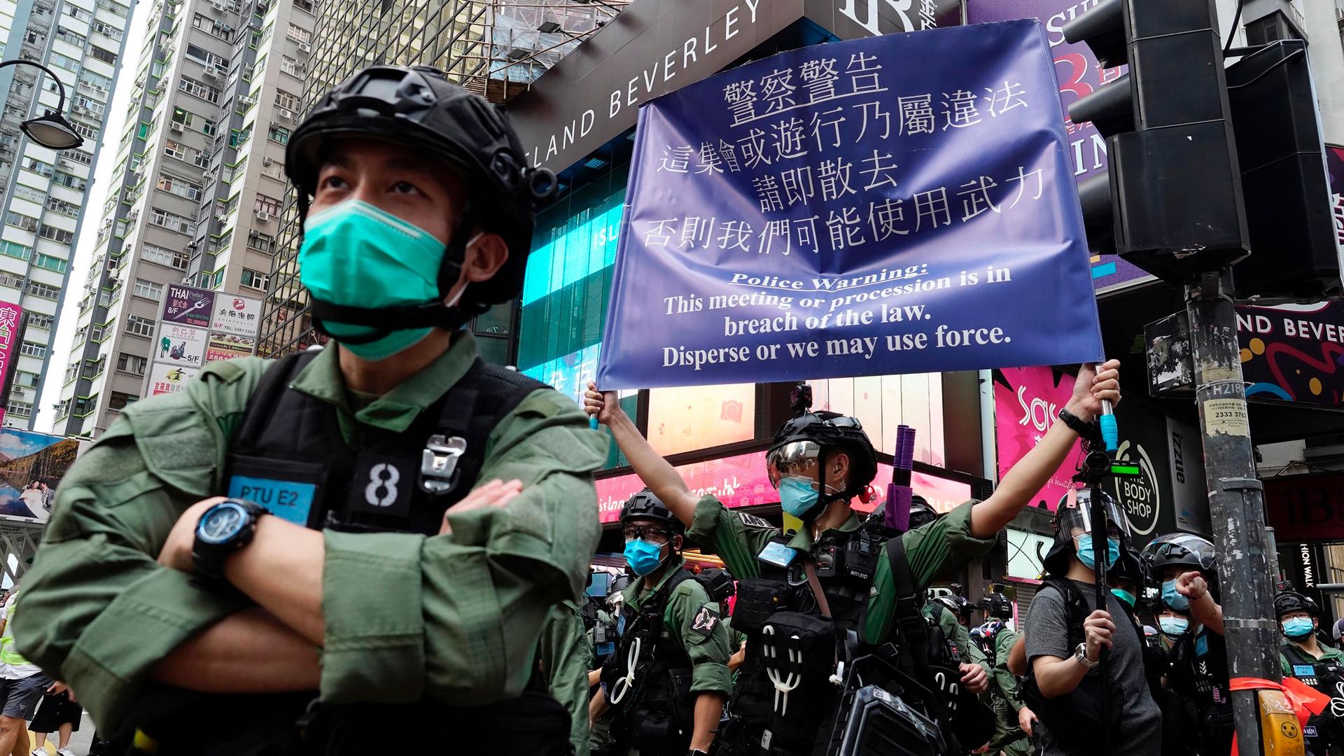 Security forces in Hong Kong are shown wearing face masks and helmets with one holding up a large purple warning banner.