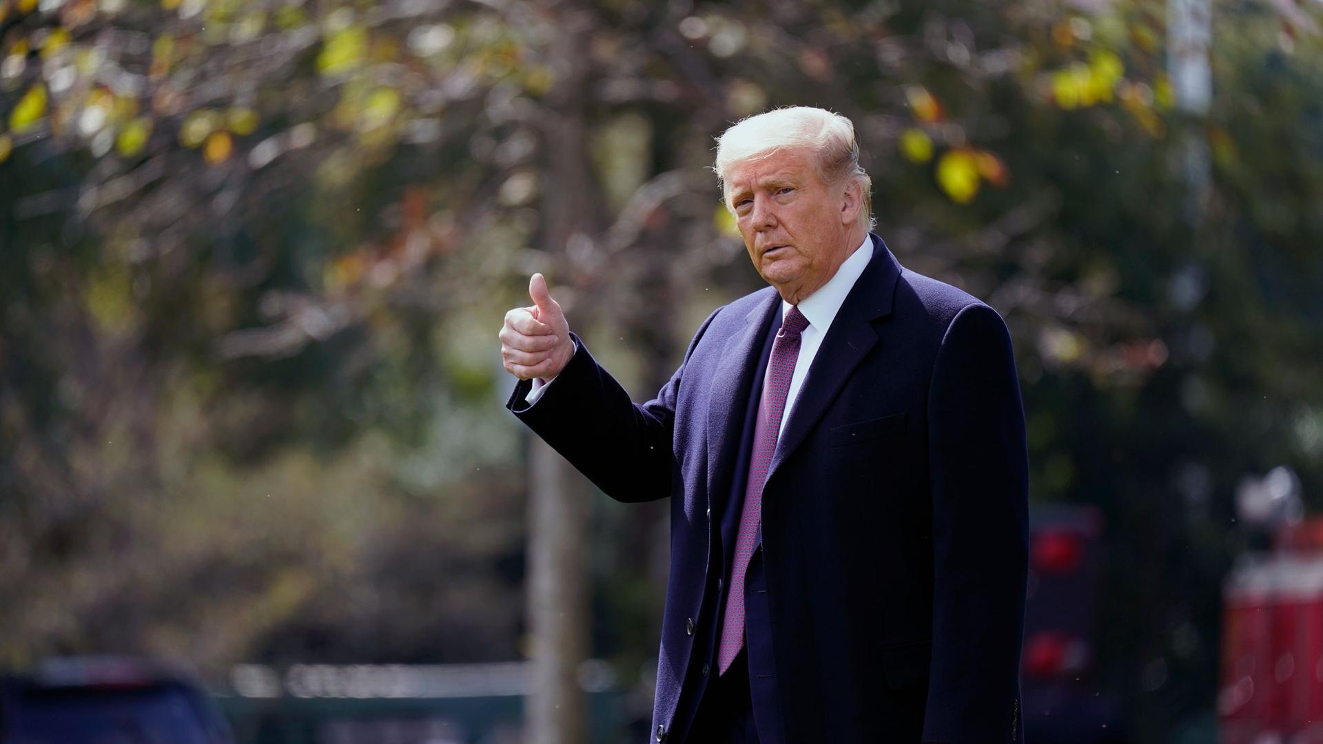 President Donald Trump is shown wearing an overcoat and purple tie and giving the thumbs-up sign.