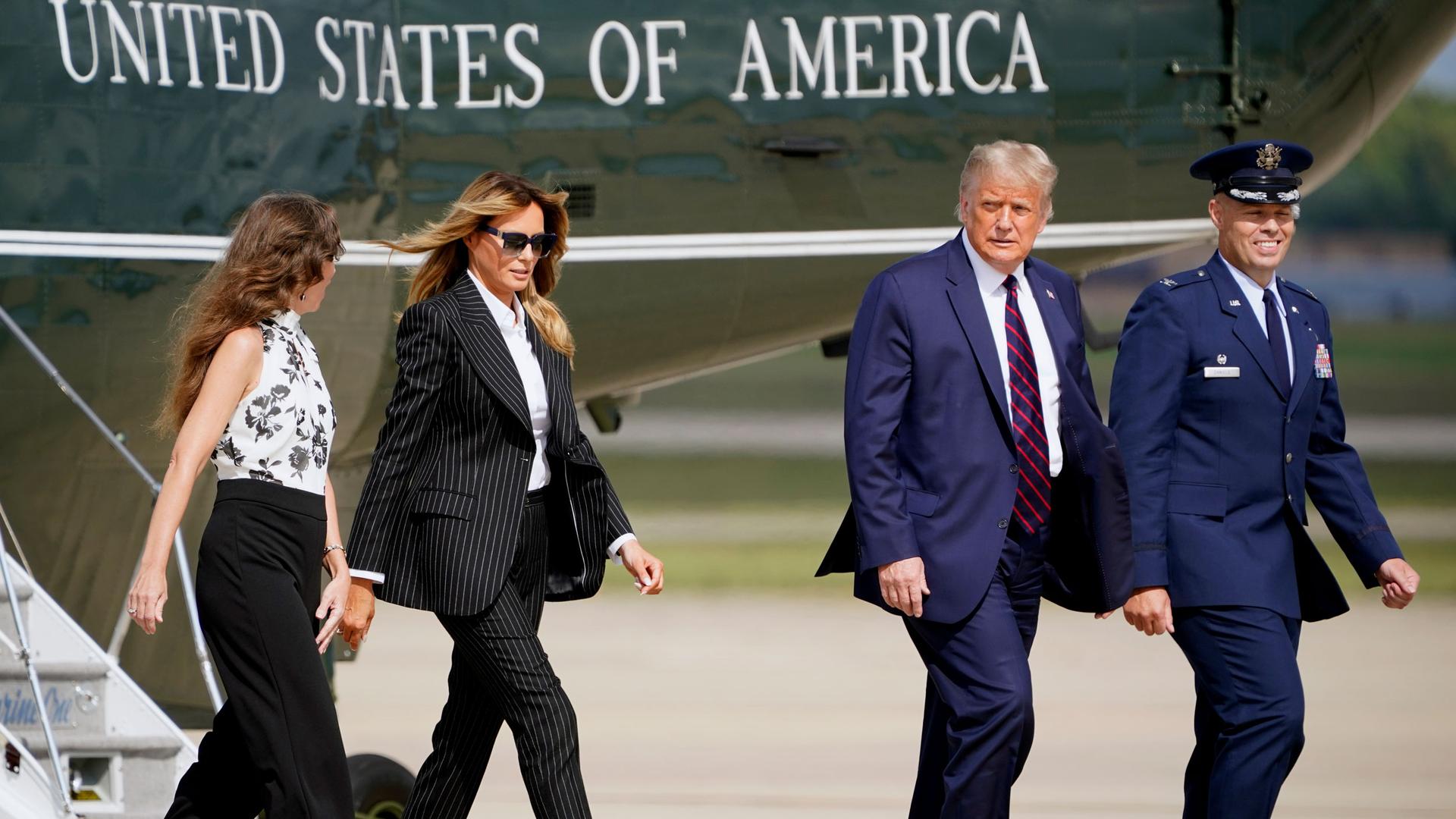 President Donald Trump and first lady Melania Trump walk are shown walking on a airport tarmac with the Marine One helicopter behind them.
