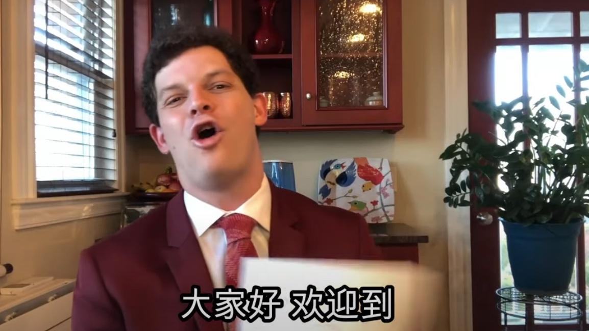 A white man wearing a suit talks in a kitchen with Chinese lettering at the bottom of the screenshot. 