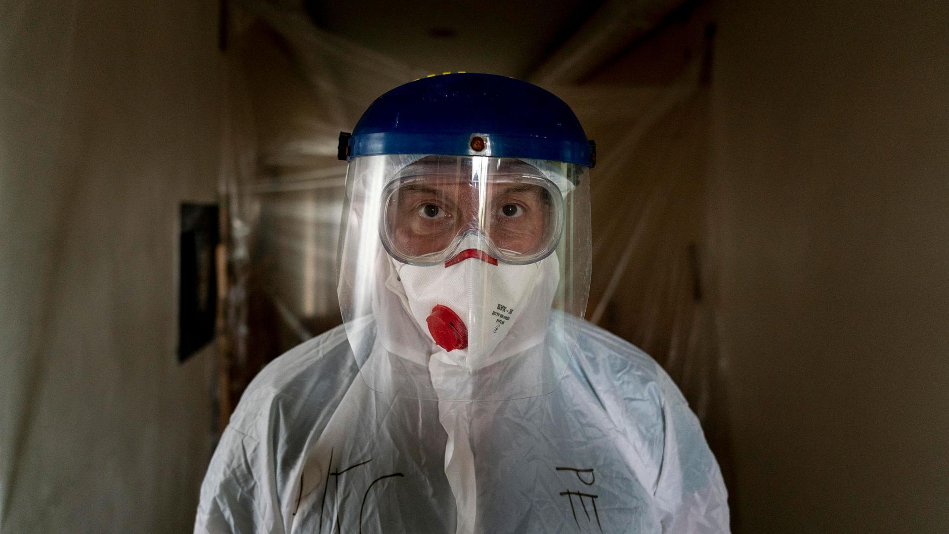 A doctor is shown looking directly into the camera and wearing goggles, a face mask and a face shield.
