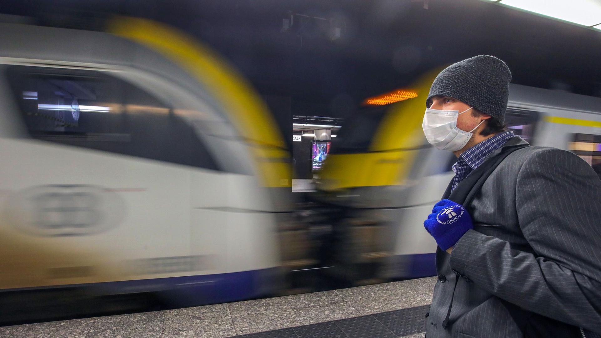 A man is shown wearing a face mask and winter hat as a train passed by in blurred motion.