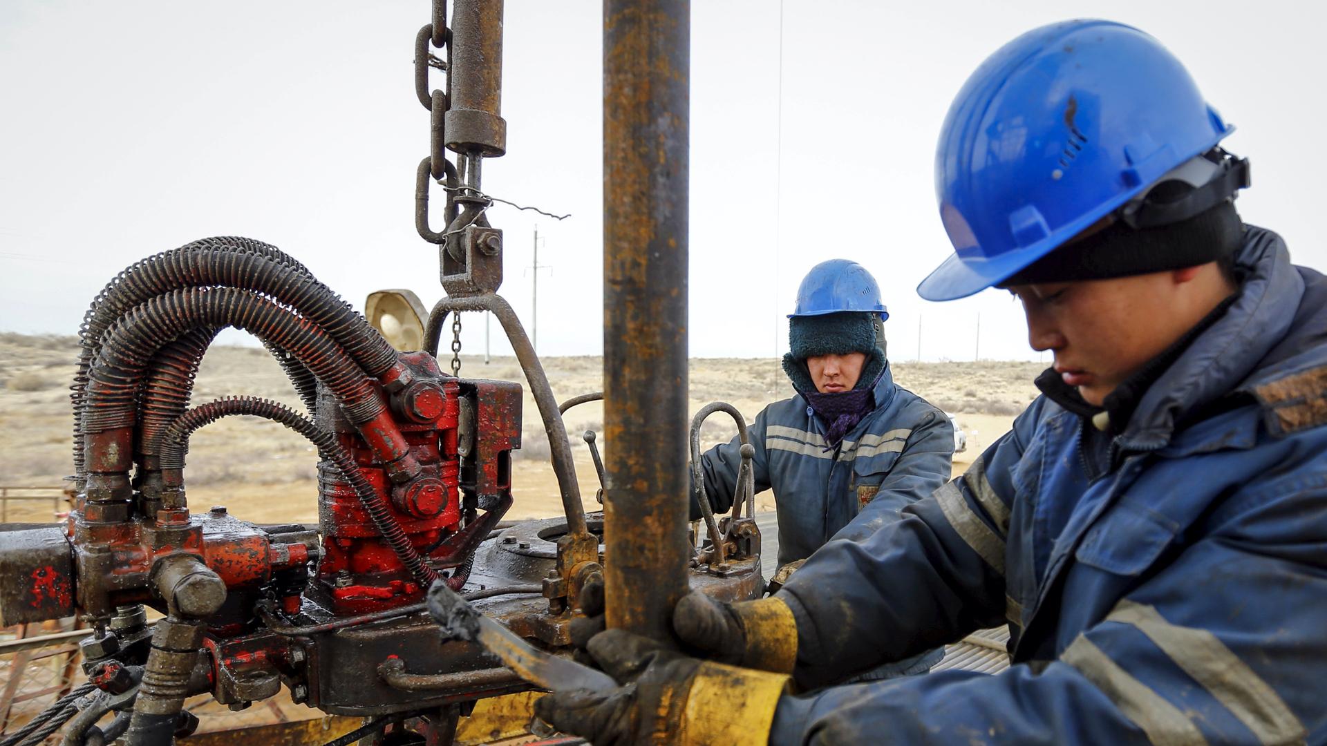 Two people wearing uniforms and blue helmets carry out maintenance at an oil well