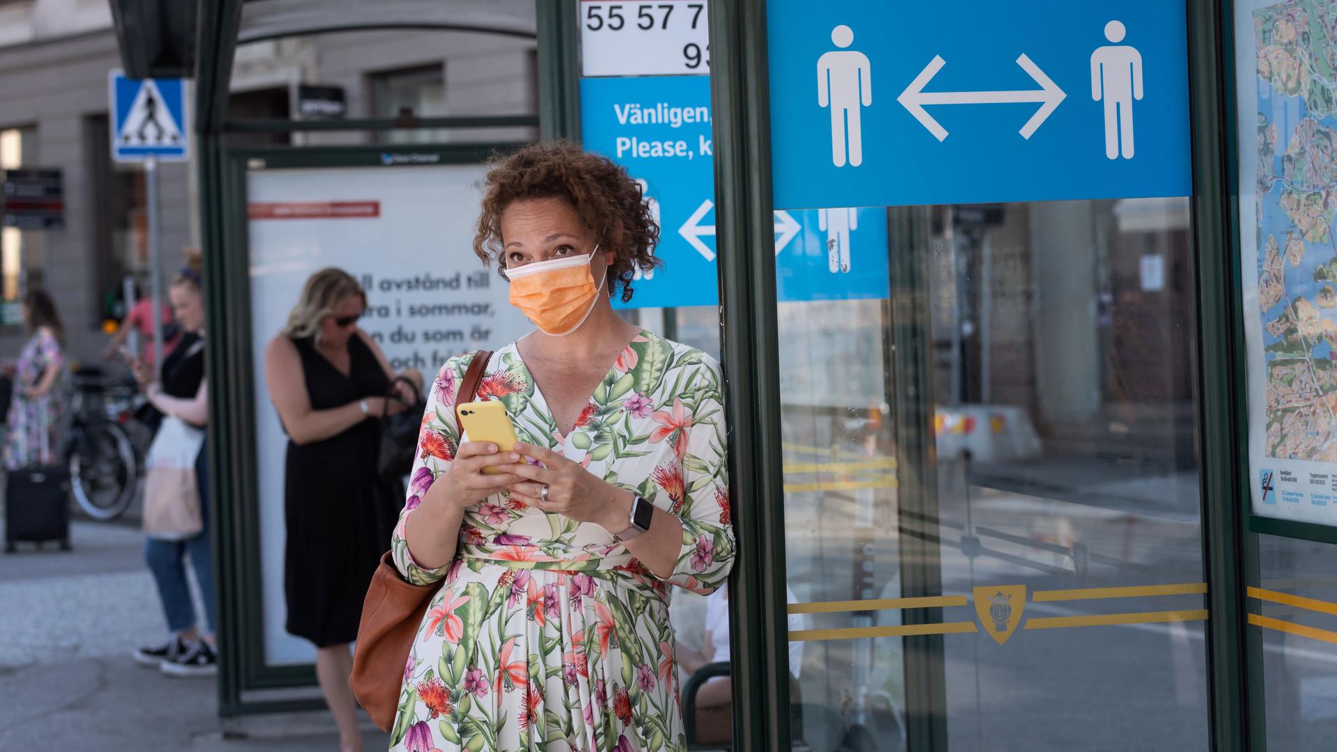 A woman wearing a face mask is seen in a bus stop next to an information sign asking people to keep social distance due to the outbreak of the coronavirus disease (COVID-19), in Stockholm, Sweden, June 26, 2020. 