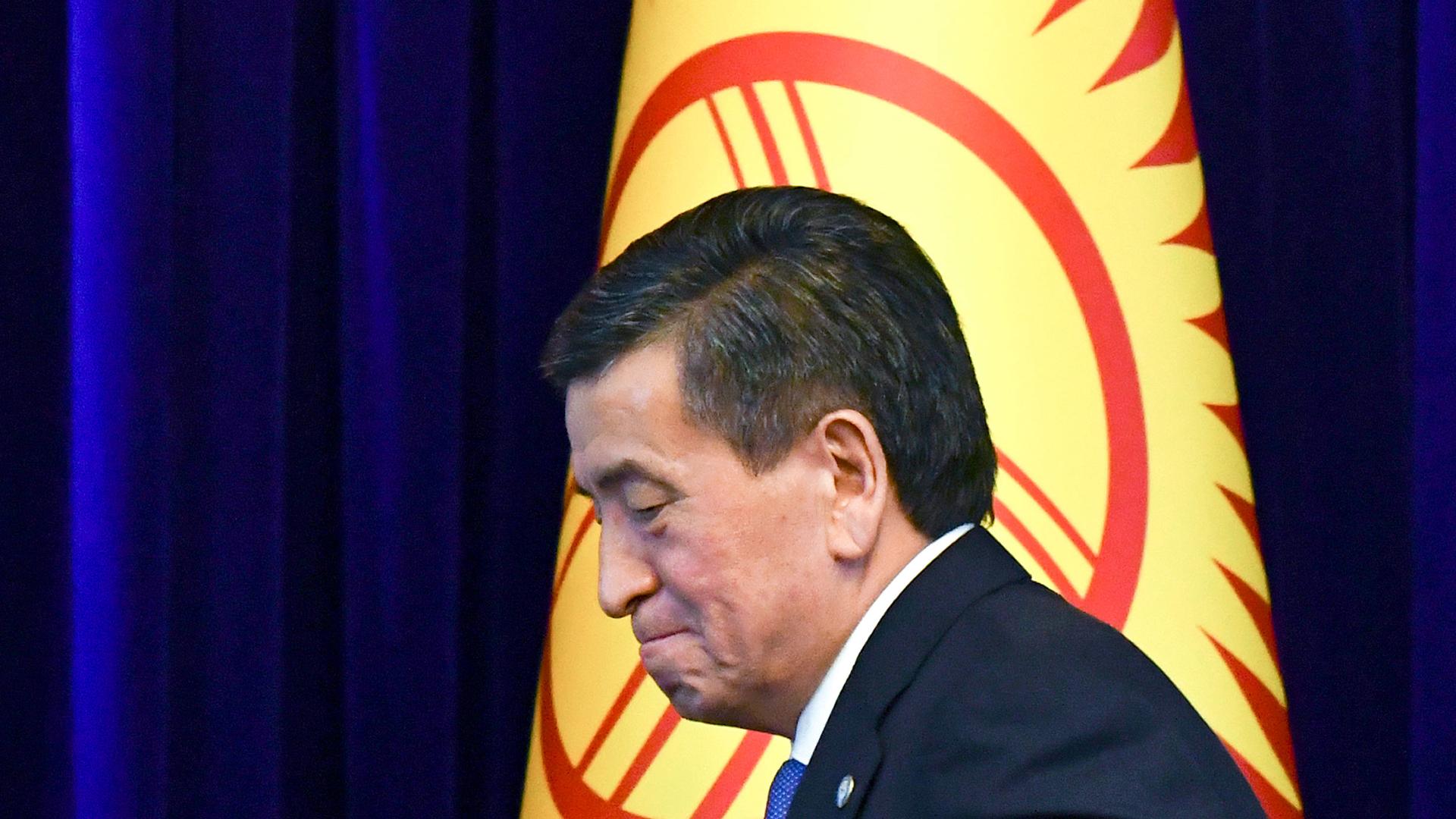 Sooronbay Jeenbekov is shown walking past the blue, yellow and red national flag.