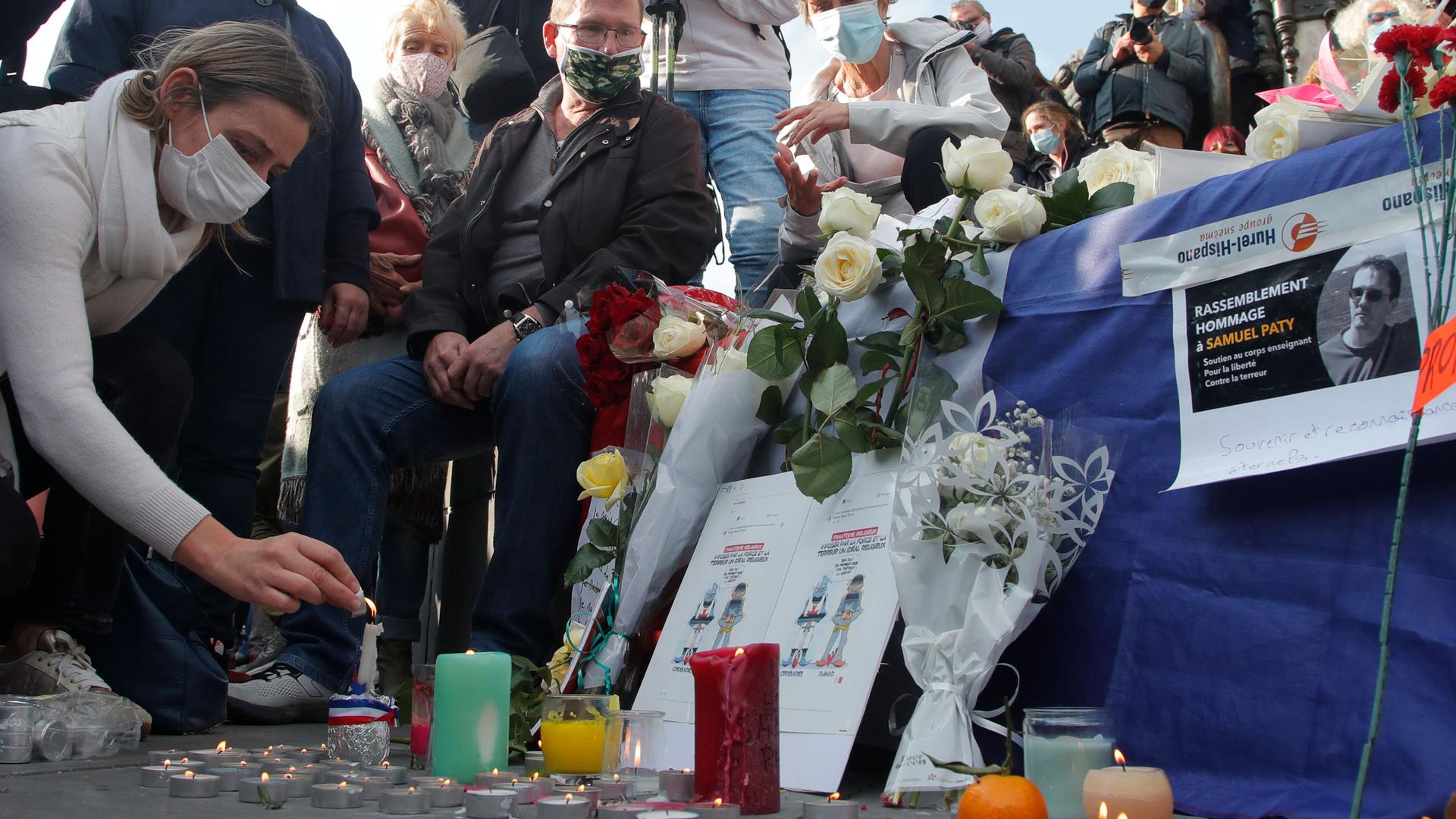 A large group of people are shown near a make shift memorial with candles and flowers for a teacher who was killed in France.