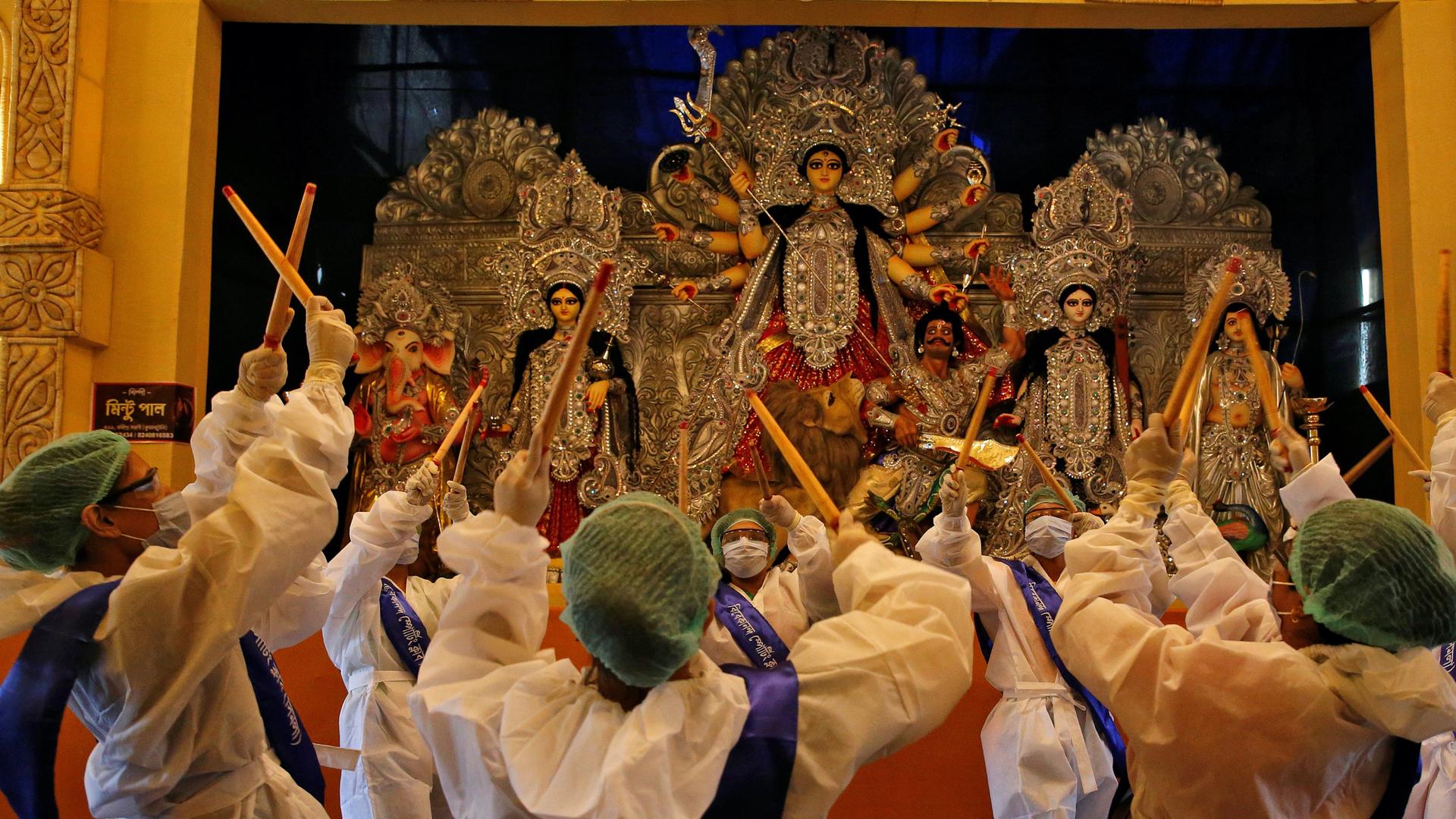 People wearing protective gear worship in front of a 10-armed ornate goddess idol on a platform. 