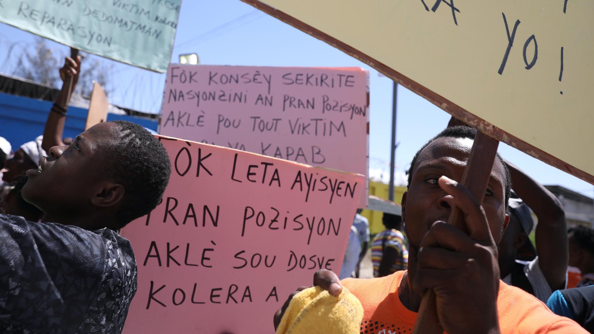 Two Haitians protest with a pink sign against UN peacekeeping mission that caused a massive cholera epidemic. 