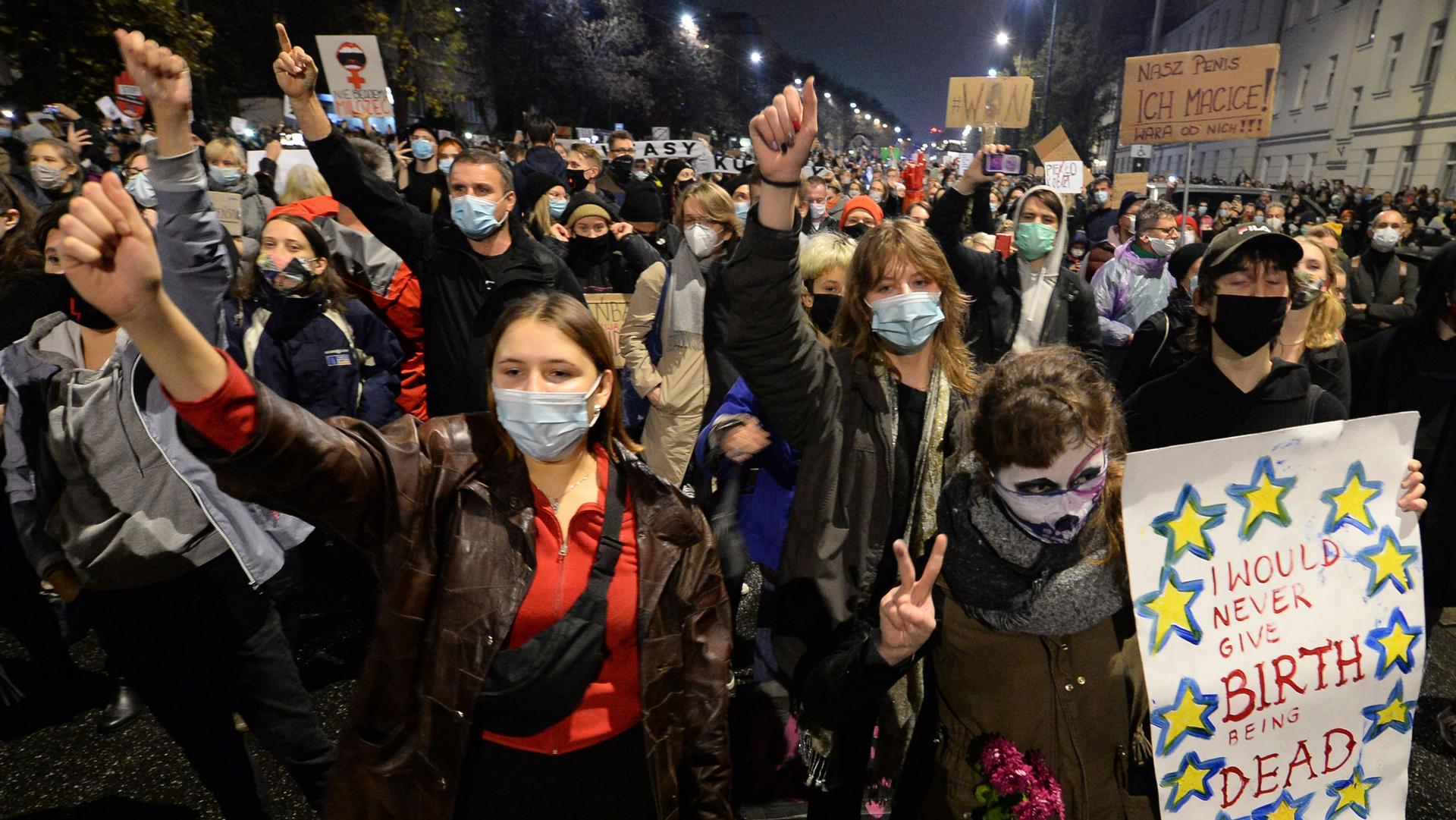 A large crowd of people are show in the street — many wearing protective face masks and carrying signs.
