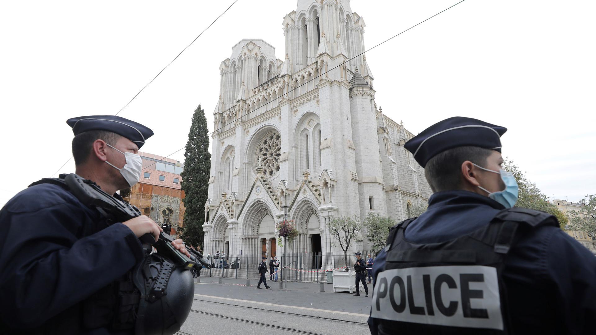 Police officers are shown standing guard across the street and holding large guns from the Notre Dame church in Nice.