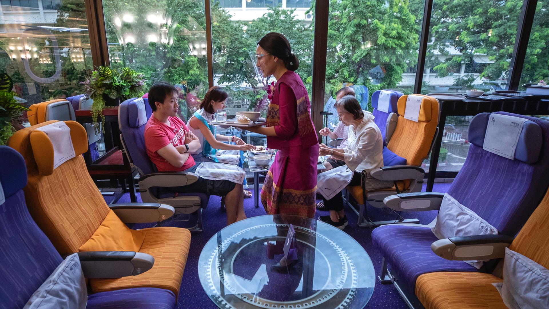 A flight attendant is serving meals in a flight-themed restaurant complete with airline seats and cabin crew to customers at Thai airways head office in Bangkok, Oct. 3, 2020. 