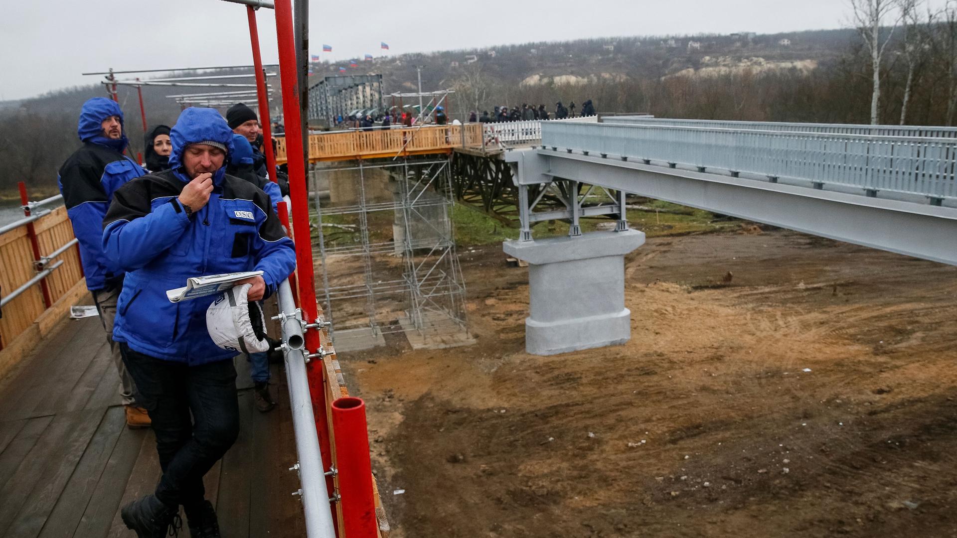 Members of Organization for Security and Cooperation in Europe (OSCE) look on as they visit a section of the restored bridge, which was blown up during a military conflict between Ukrainian government forces and Russian-backed rebels, in the settlement of