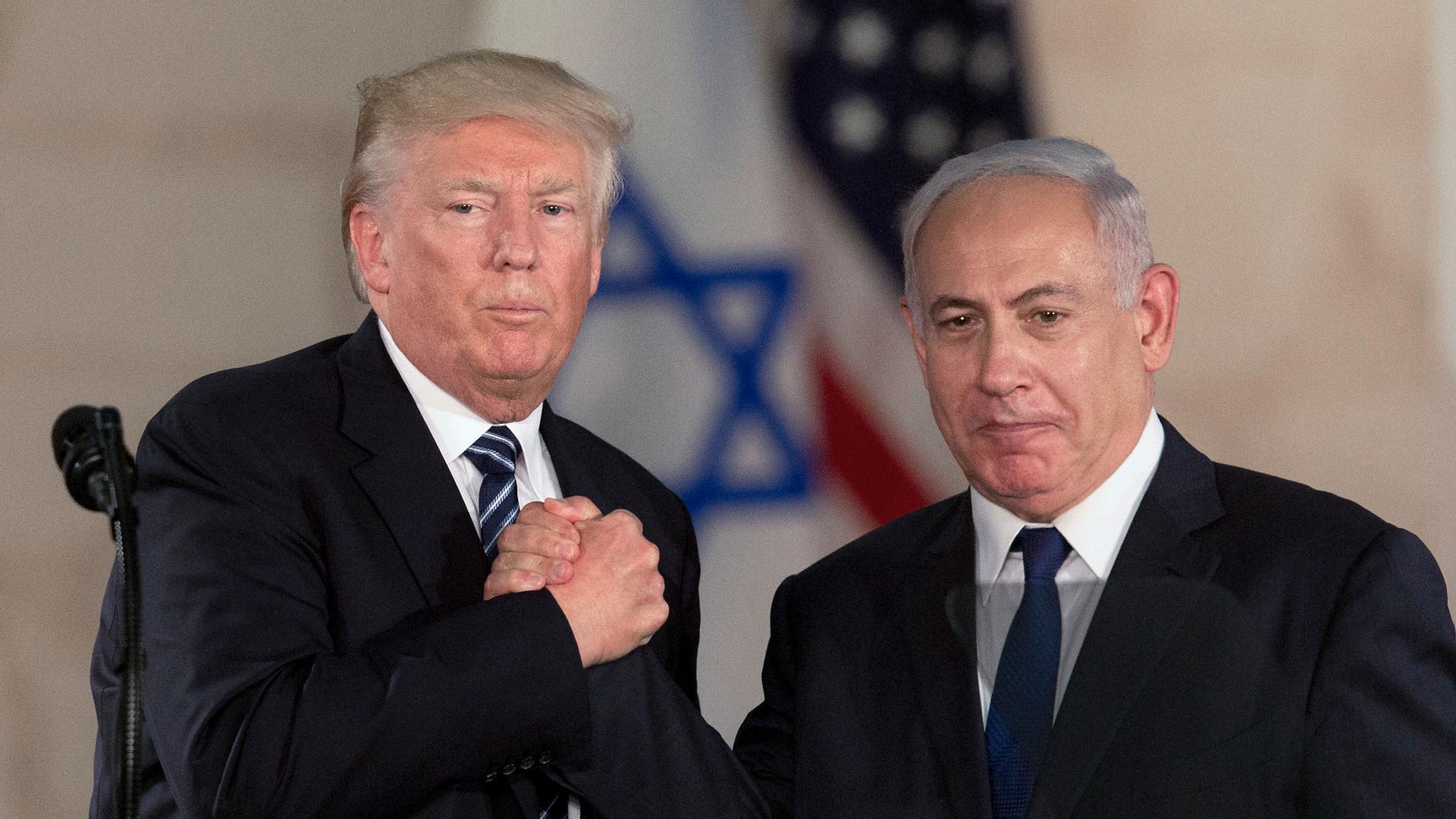 US President Donald Trump and Israeli Prime Minister Benjamin Netanyahu are shown both wearing dark suits and in a tight handshake.