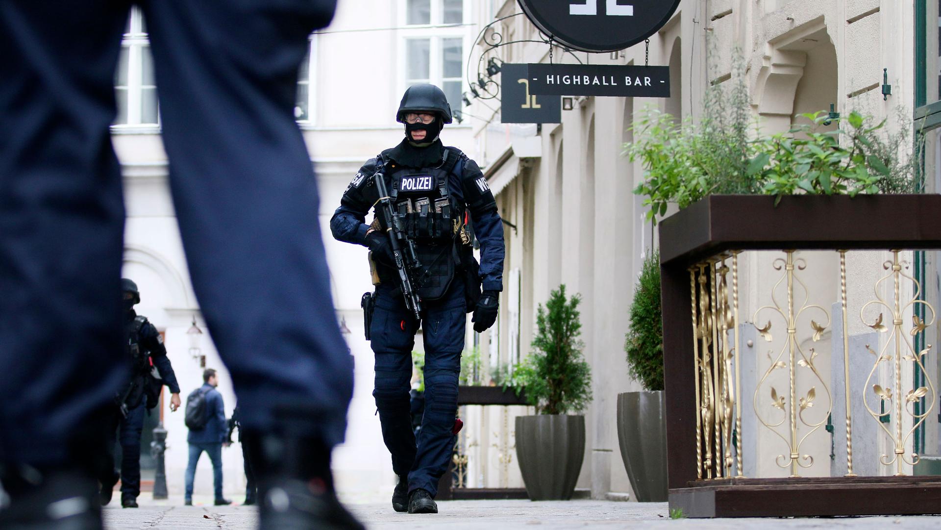 Several heavily armed police officers are shown walking on a street in Vienna with one officer passing a bar.