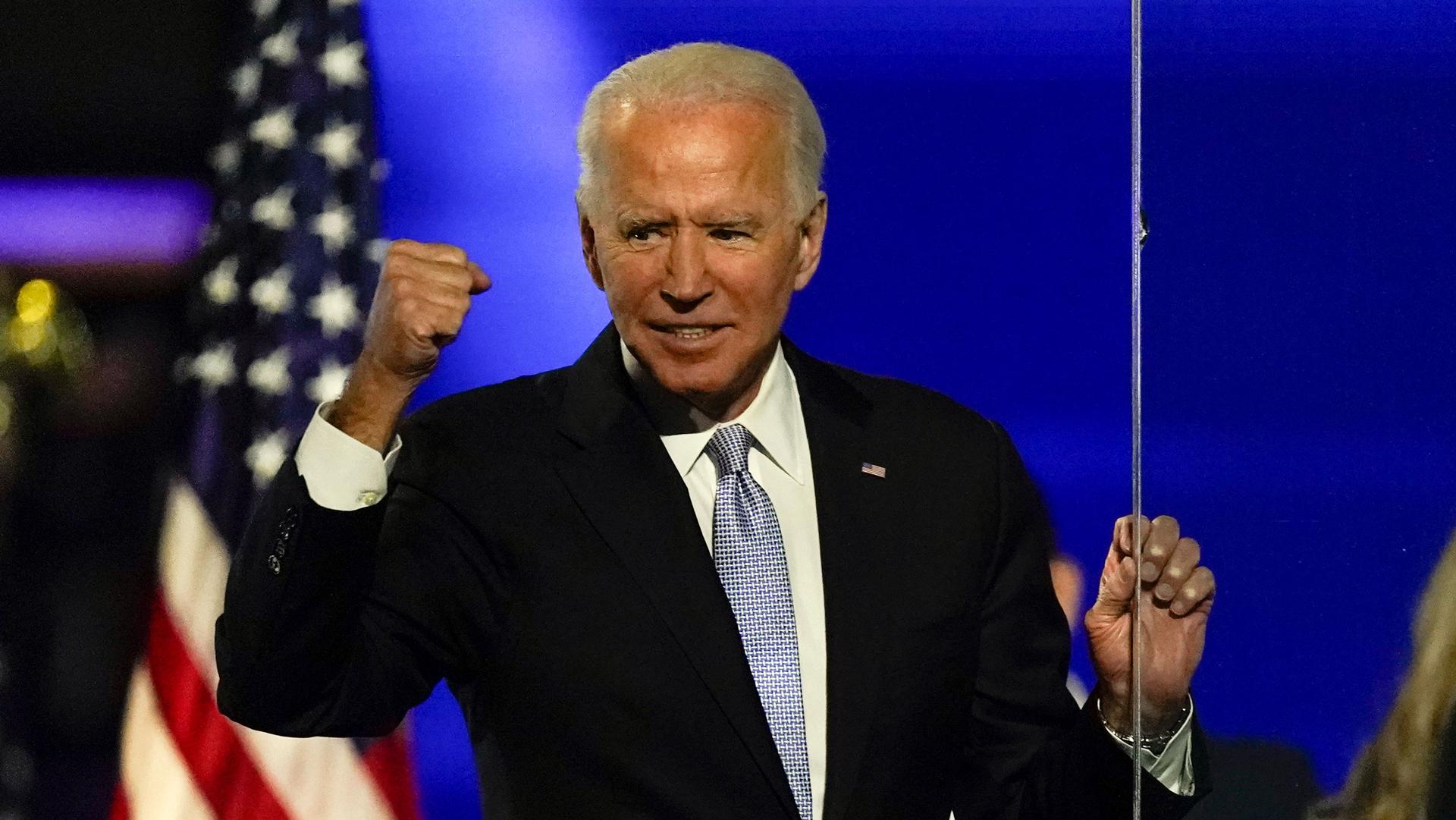 President-elect Joe Biden is shown wearing a dark suit and smiling while holding his fist in the air.